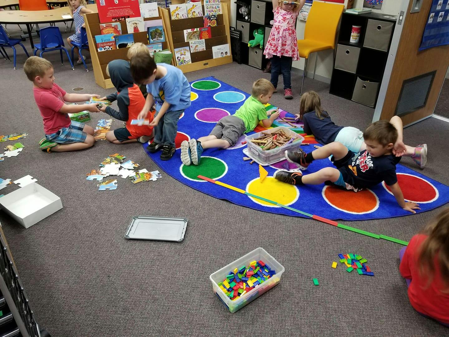 Children playing with puzzles and toys on a colorful mat in a classroom