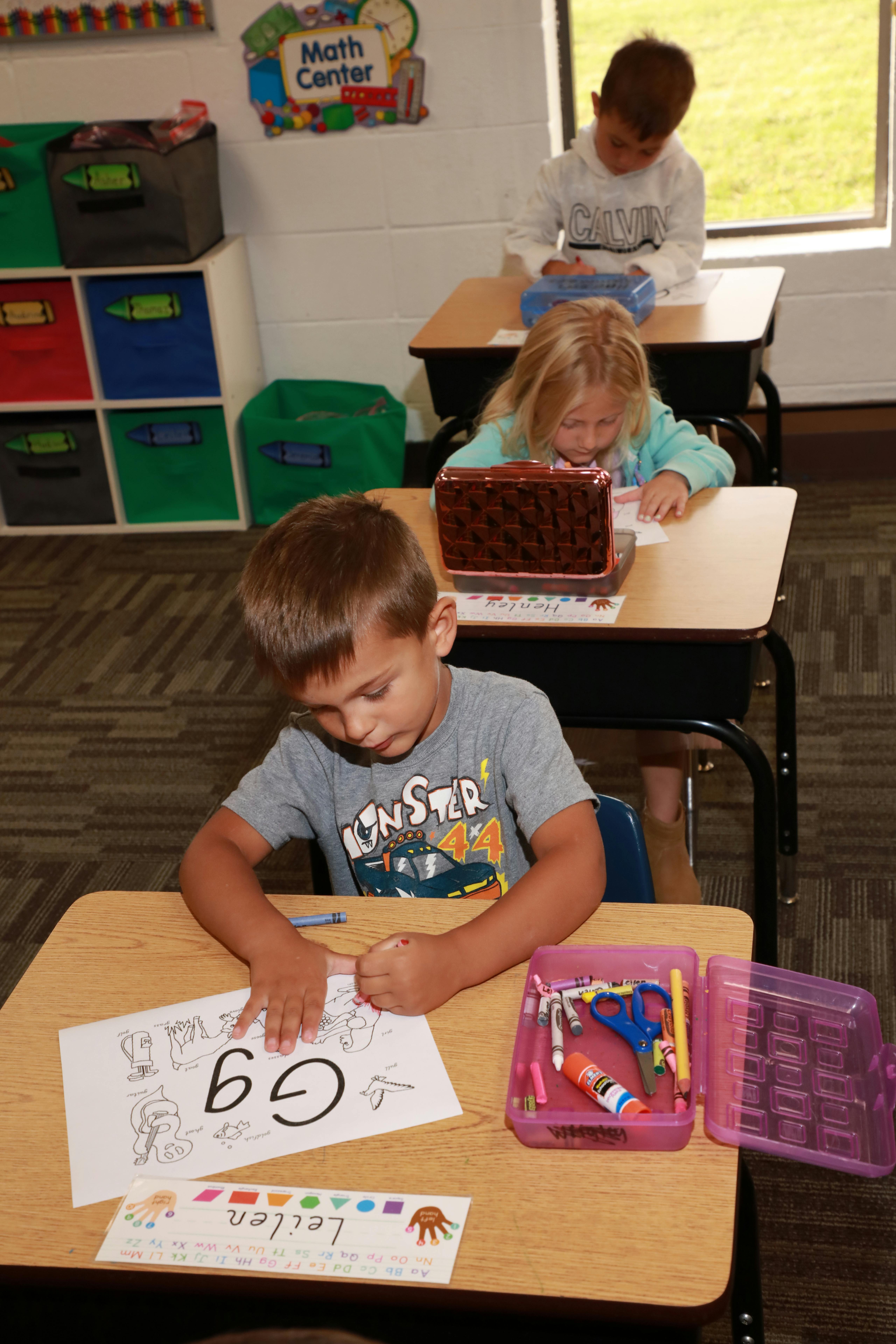 Children sitting at desks in a classroom, working on papers