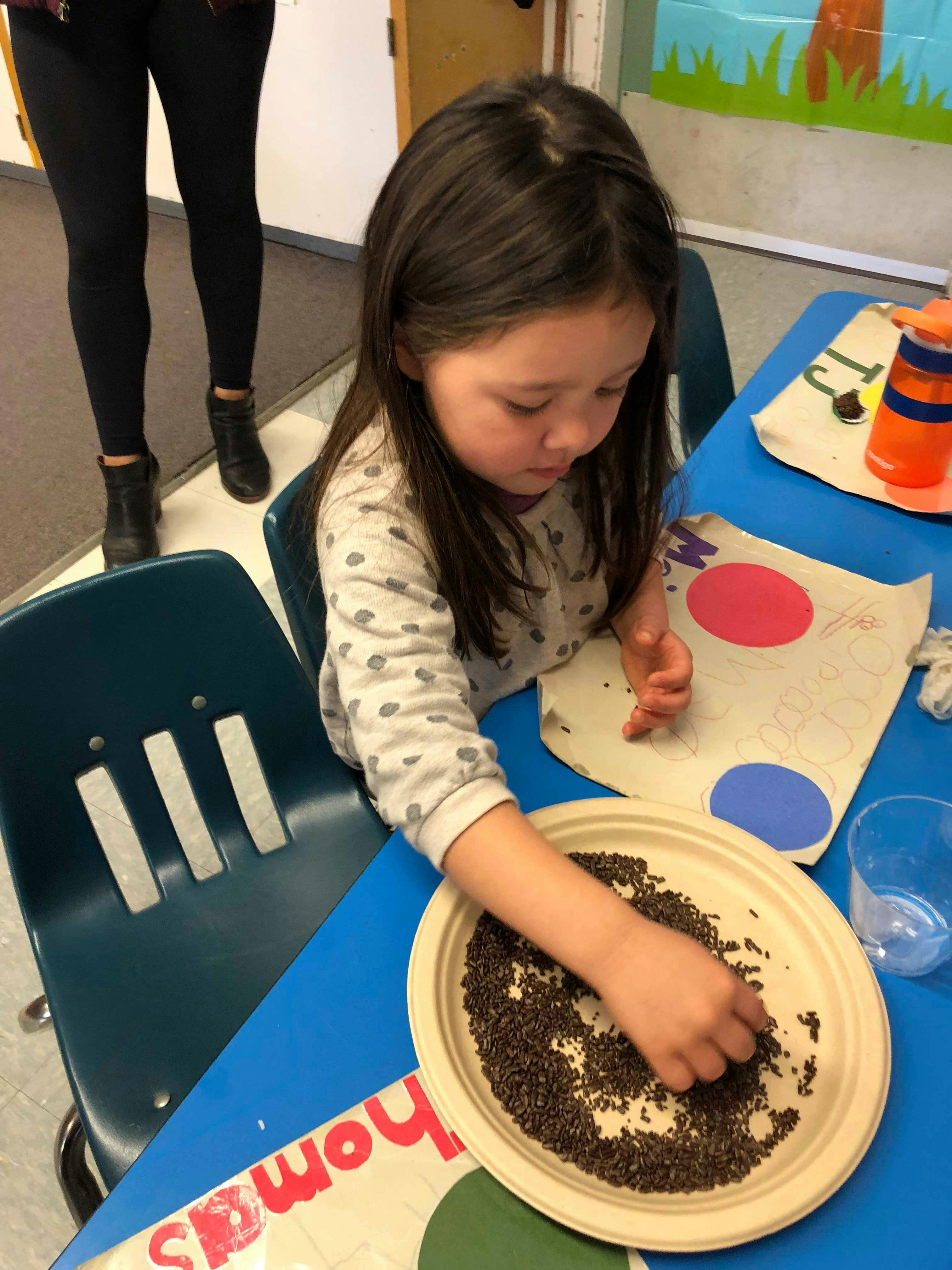 Child sitting at a table, reaching into a plate of small dark objects