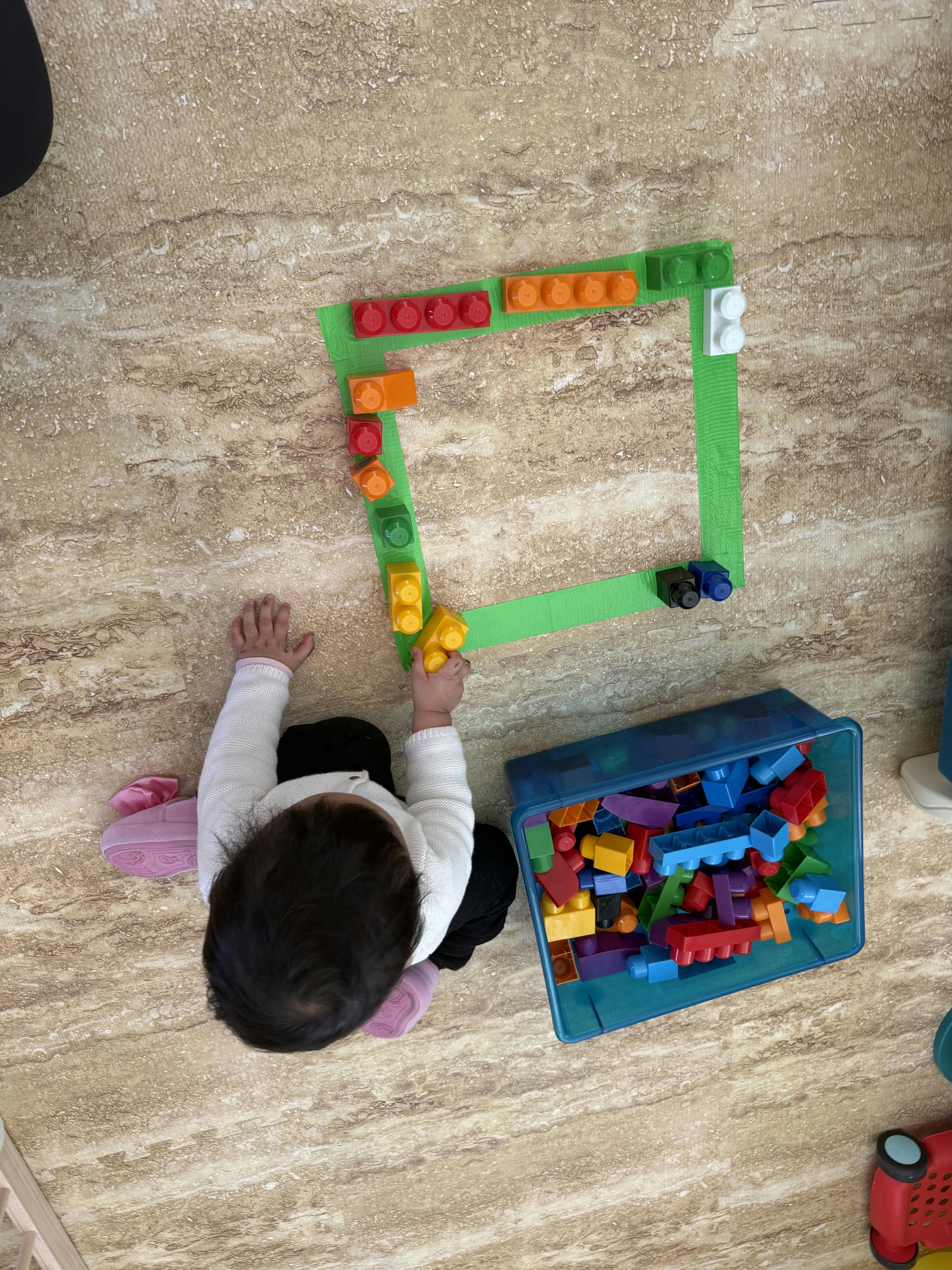 Child playing with large building blocks, forming a square on the floor