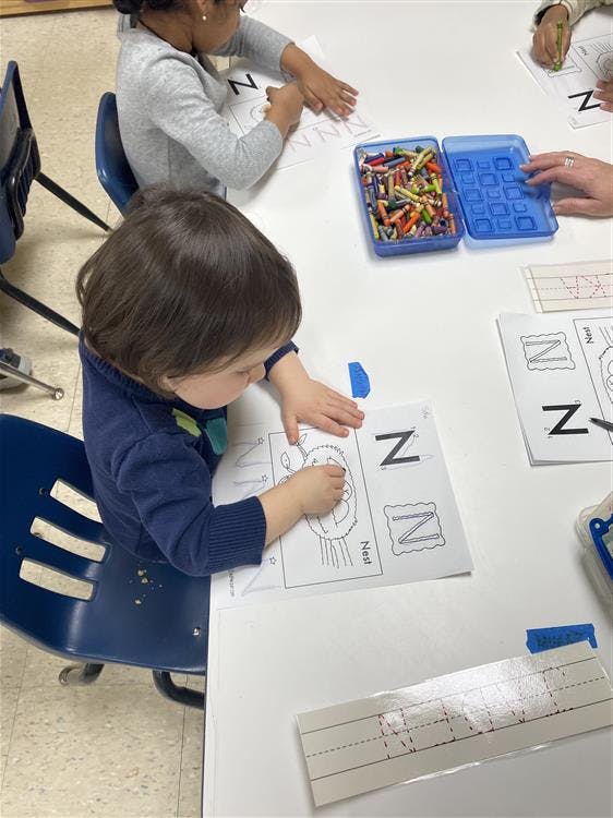 Child coloring an image with the letter N next to it at a table with other children