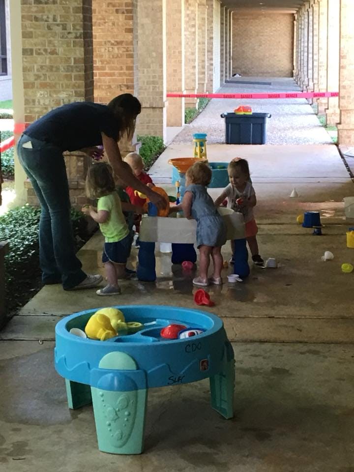 Person and multiple children playing with water tables outdoors