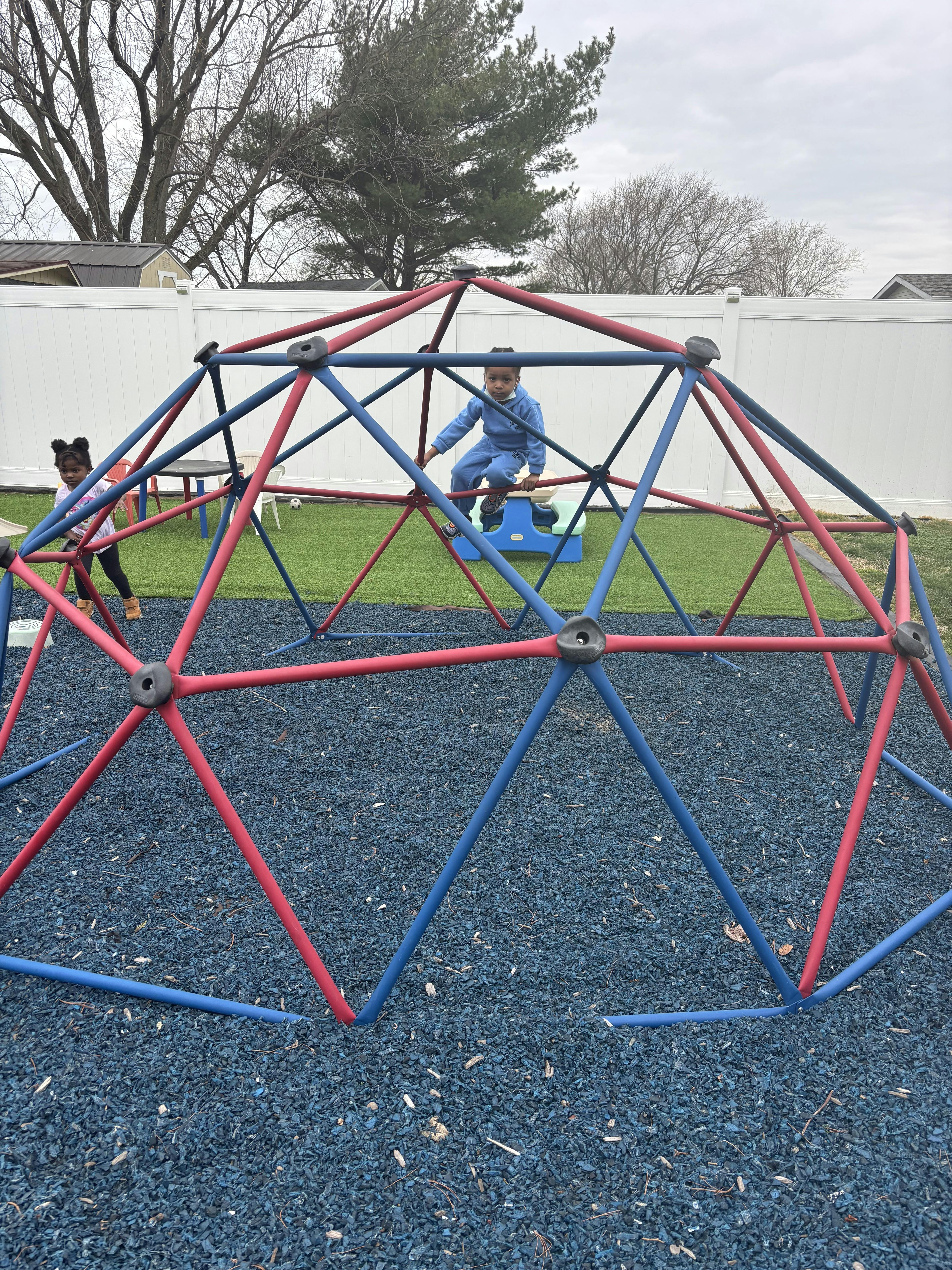 Two children playing on a red and blue climbing dome outdoors