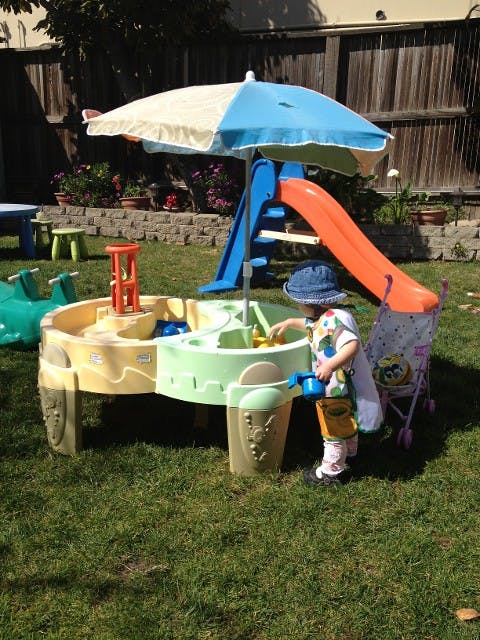 Child playing at a water table with an umbrella and slide in a backyard