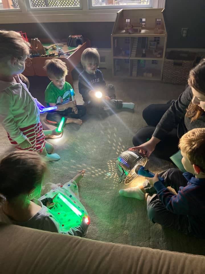 Adult and children sitting on floor with flashlights and light-up toys