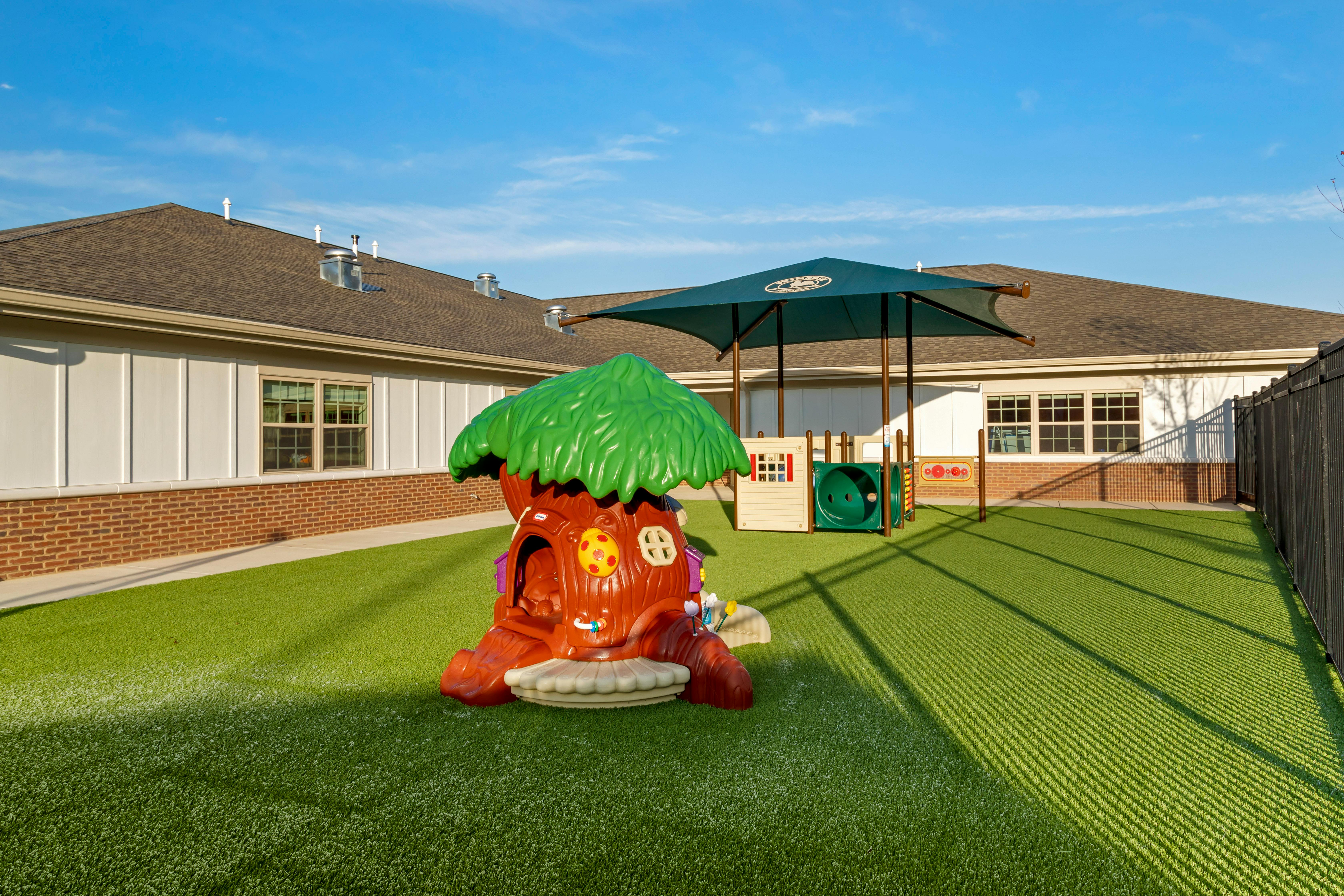 Children's playground with a treehouse structure and play equipment under a canopy