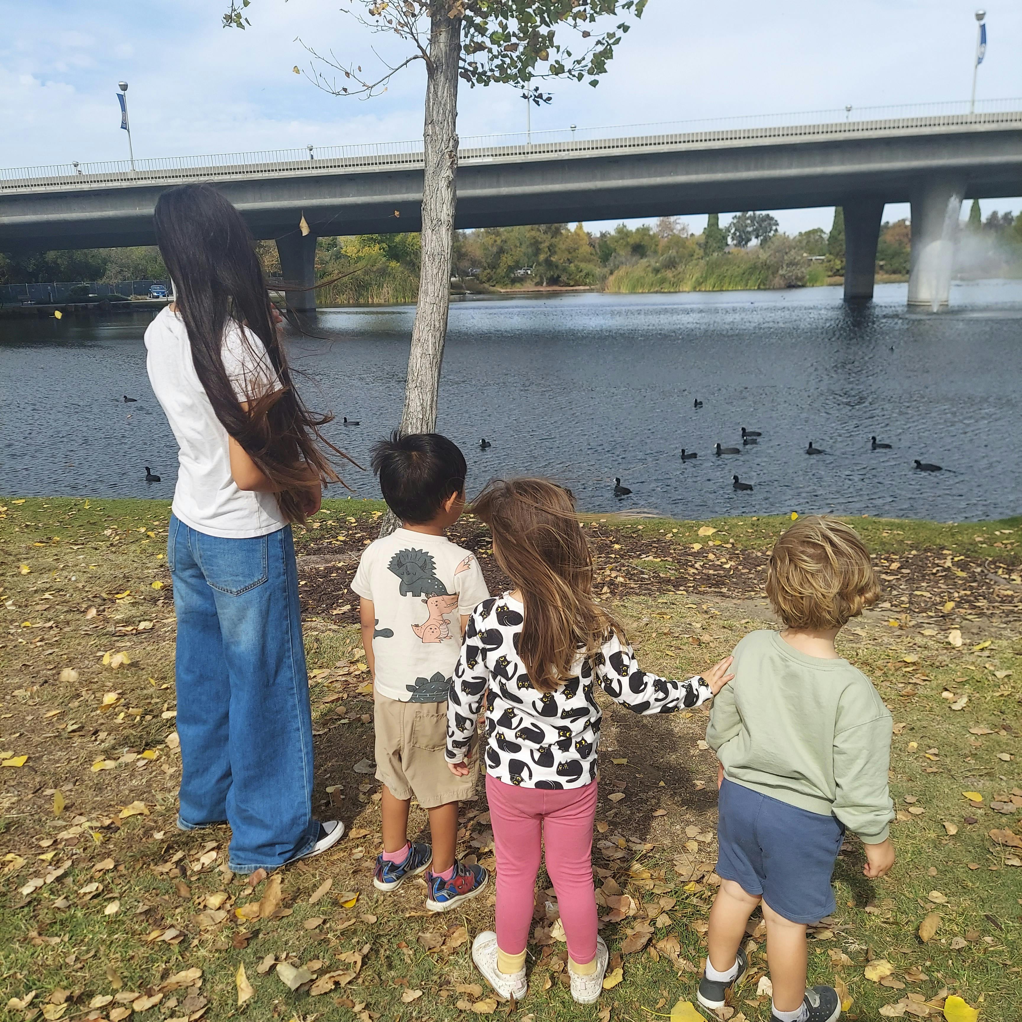 Person and three children looking at a body of water with ducks