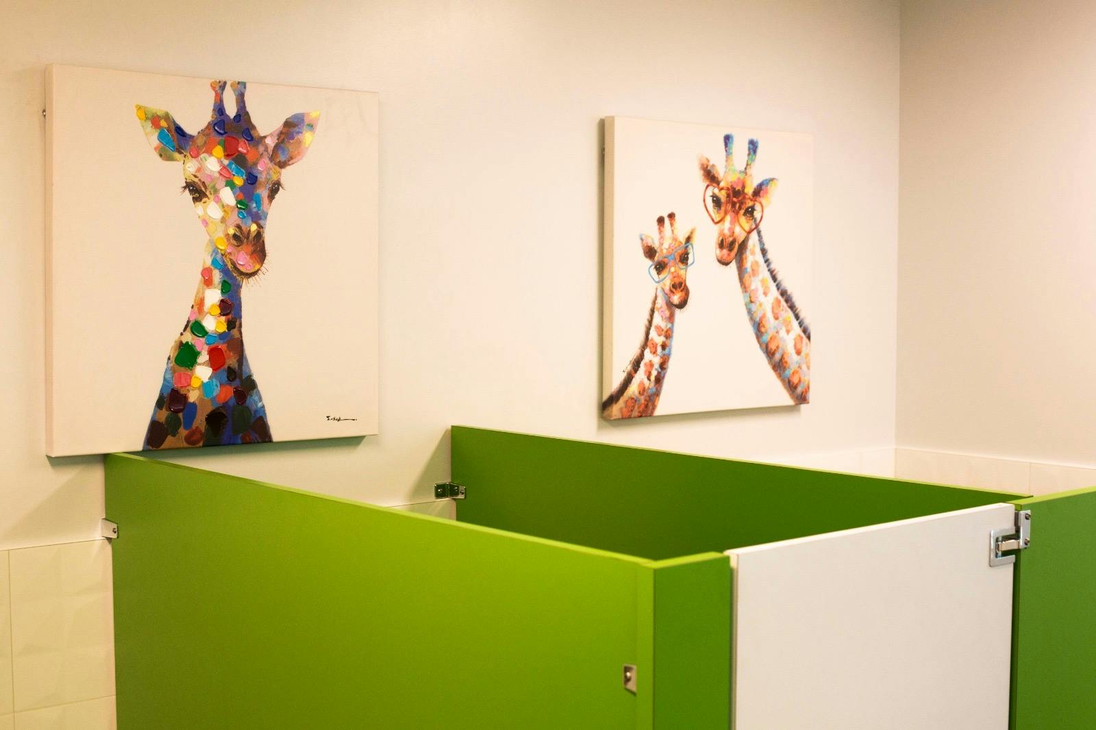 Two paintings of giraffes on a wall above green partitions