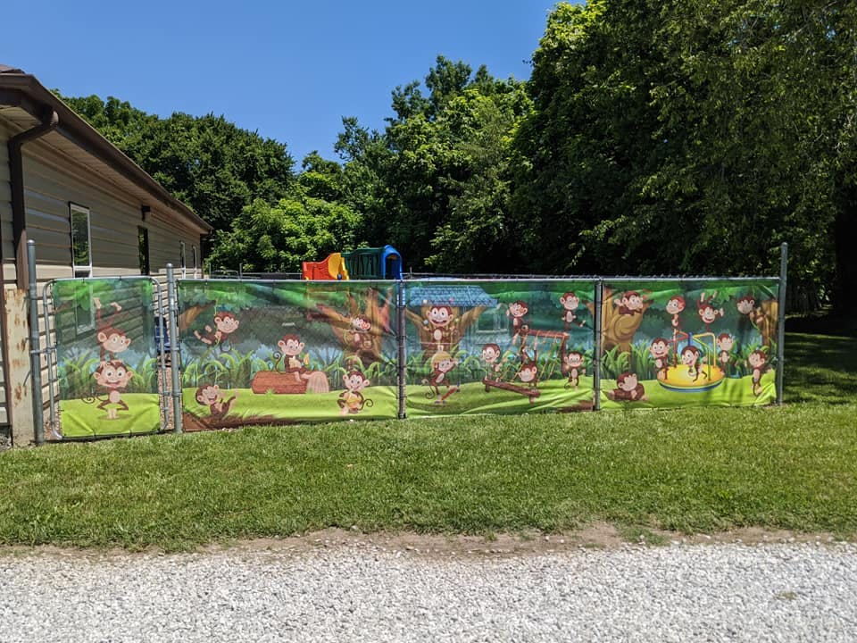 Chain link fence with a colorful banner depicting cartoon monkeys in a jungle