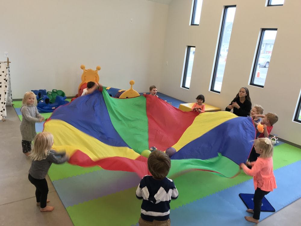 Children and an adult playing with a colorful parachute in a room