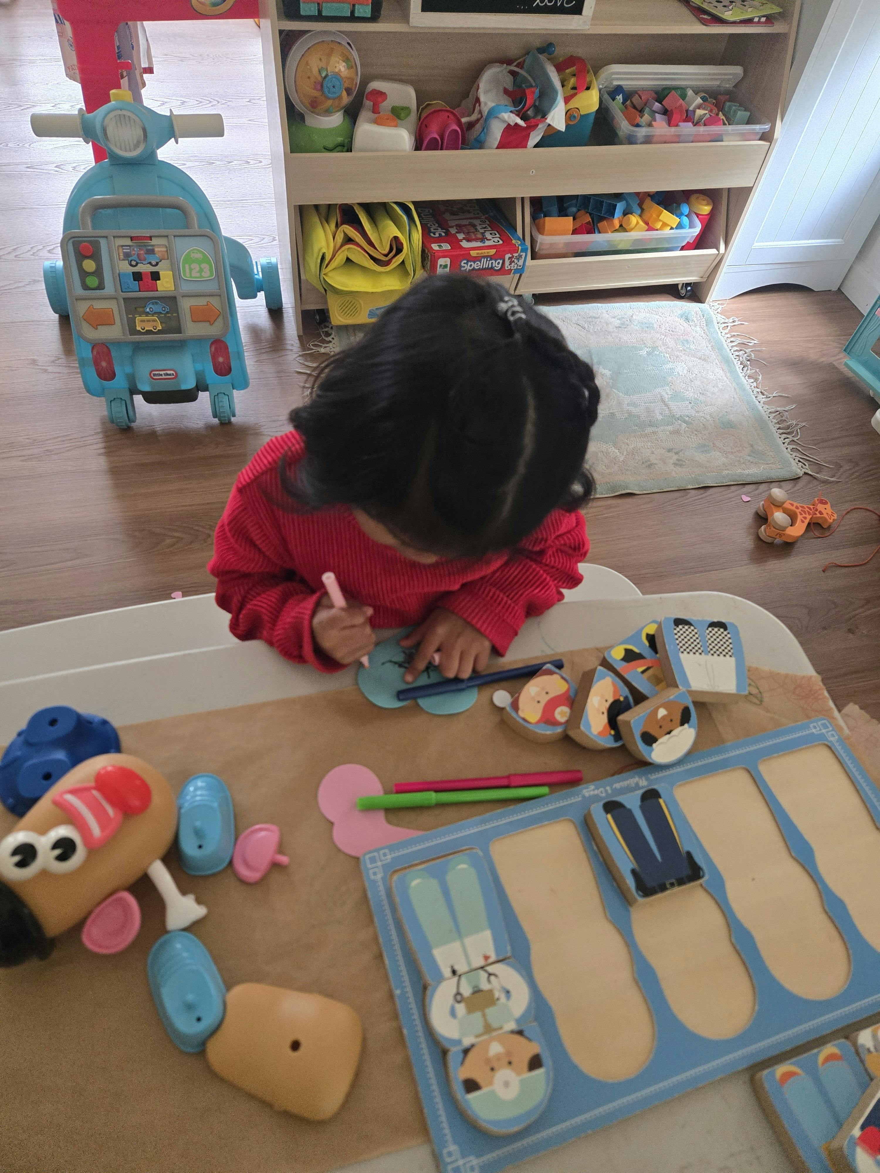 Child drawing on blue paper at a table with toys