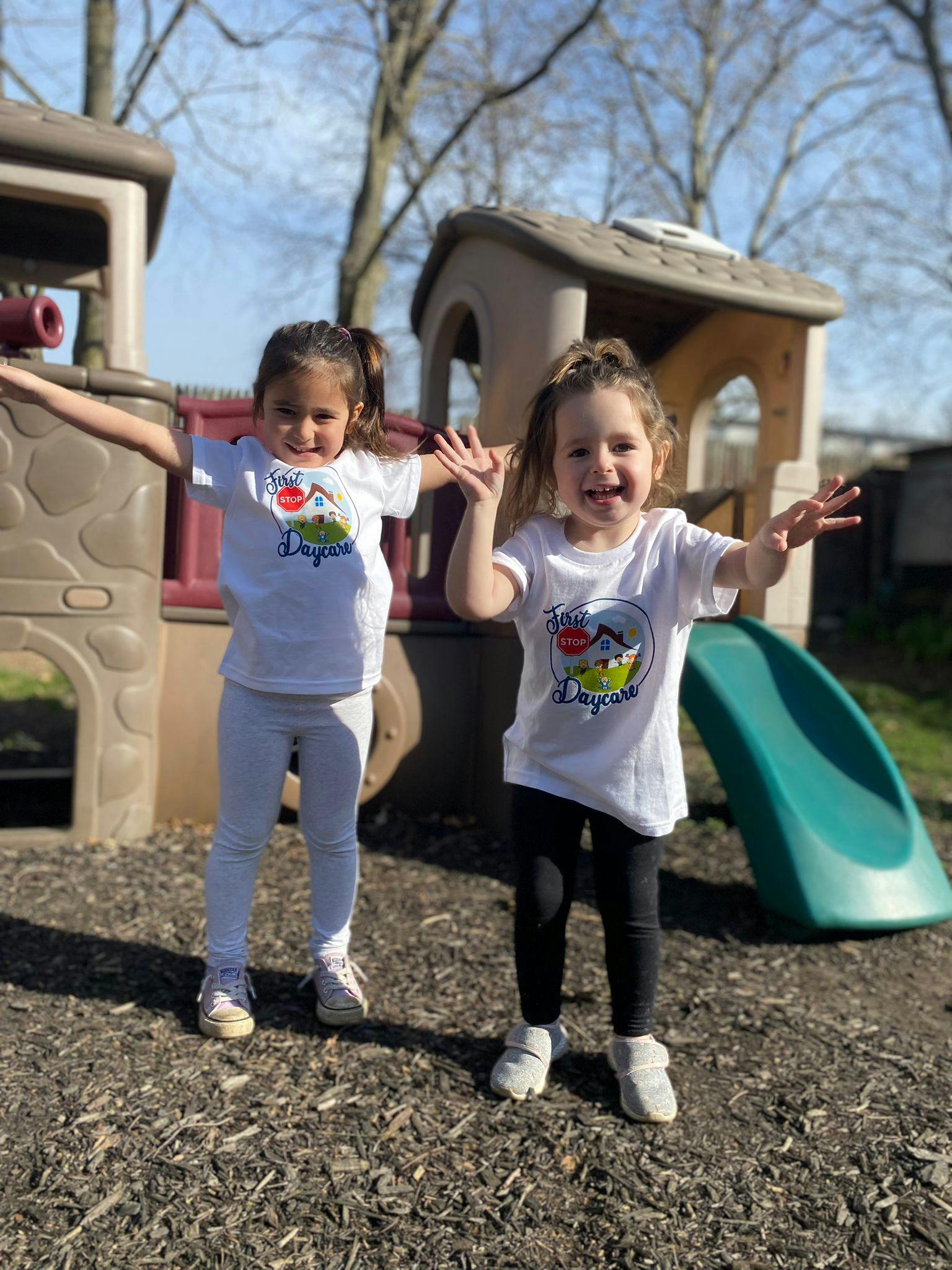Two children standing on a playground with arms outstretched