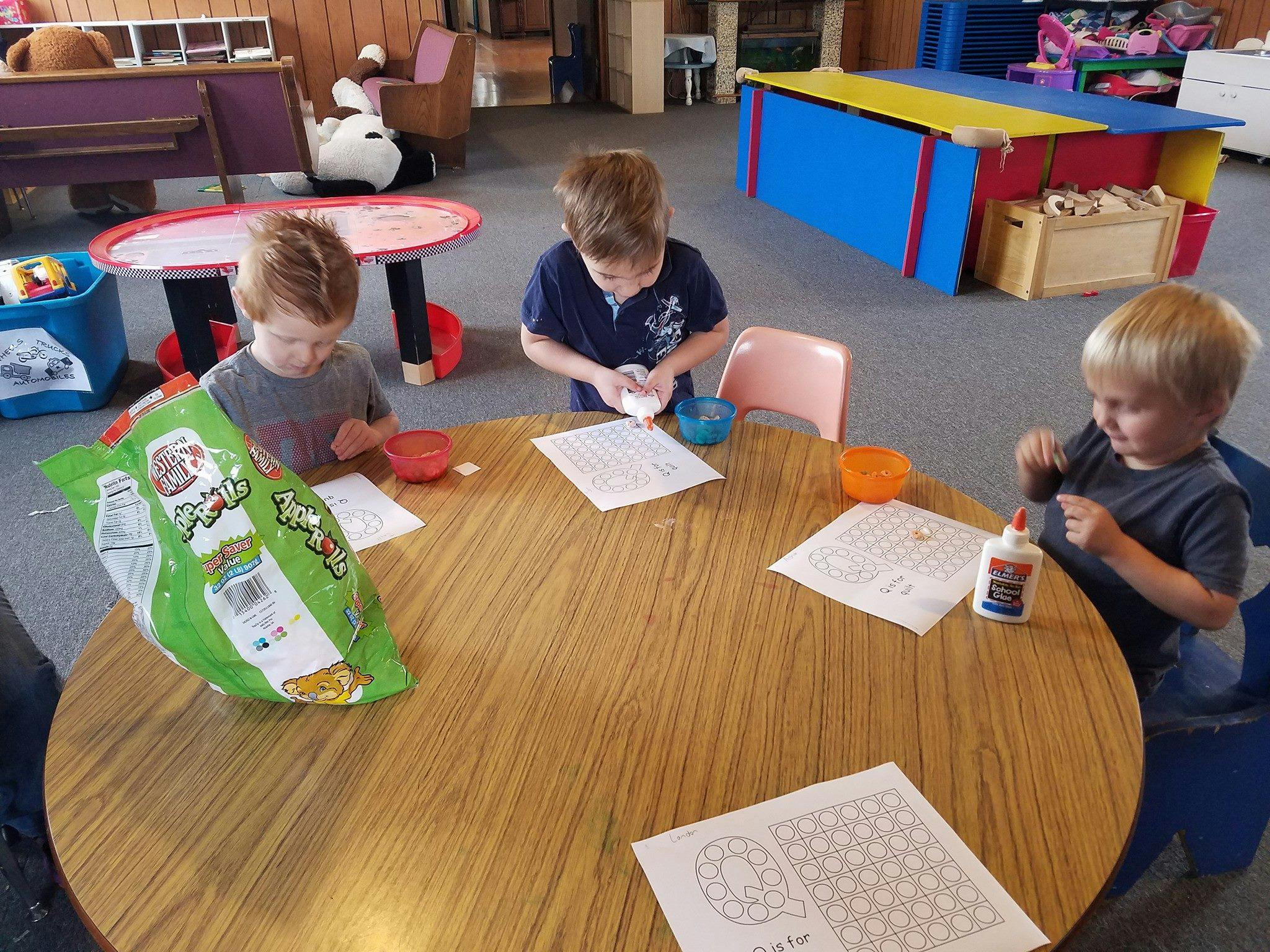 Three children at a table doing crafts with paper and glue