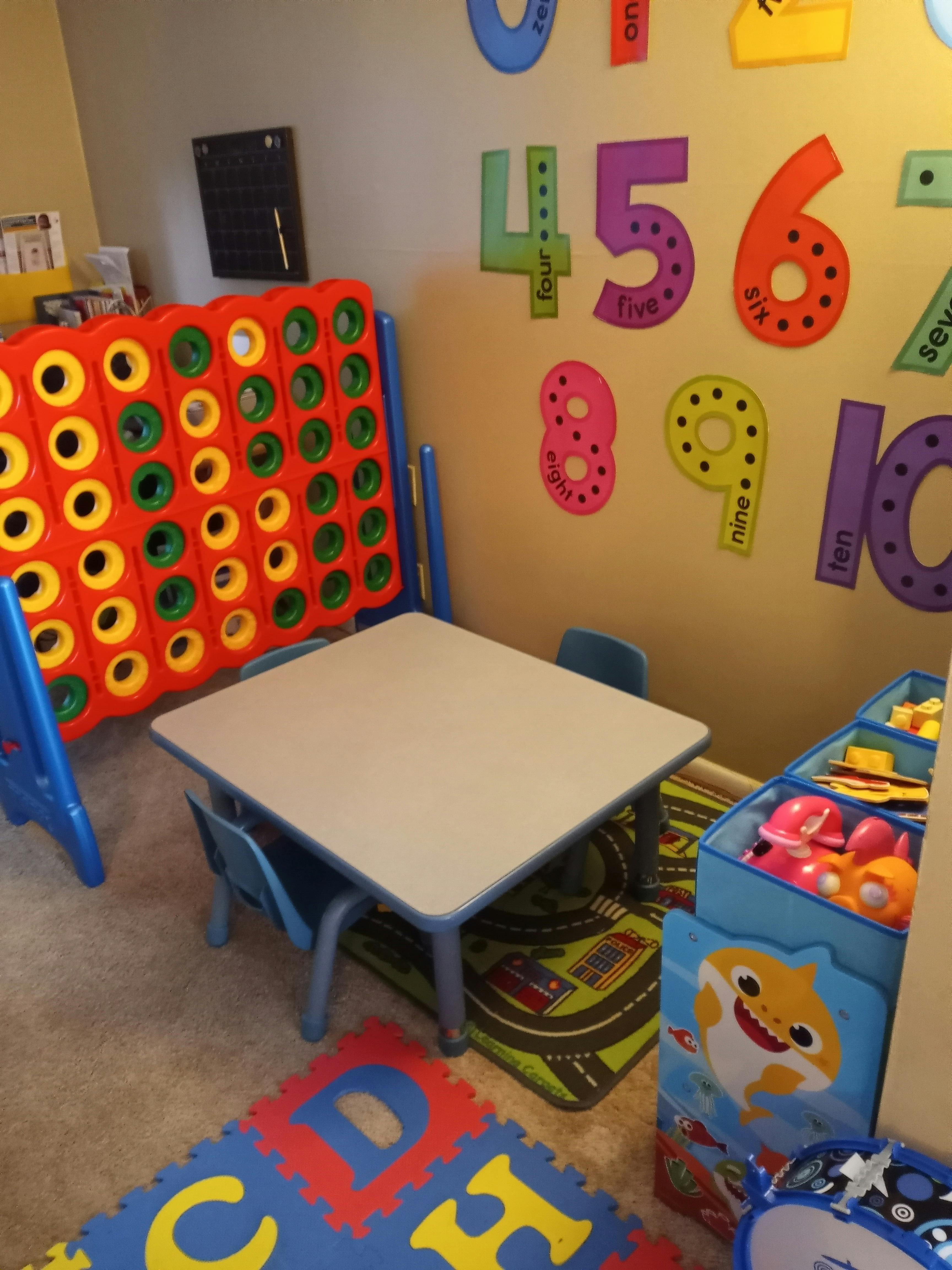 Children's play area with a table, chairs, large Connect Four game, and number decals