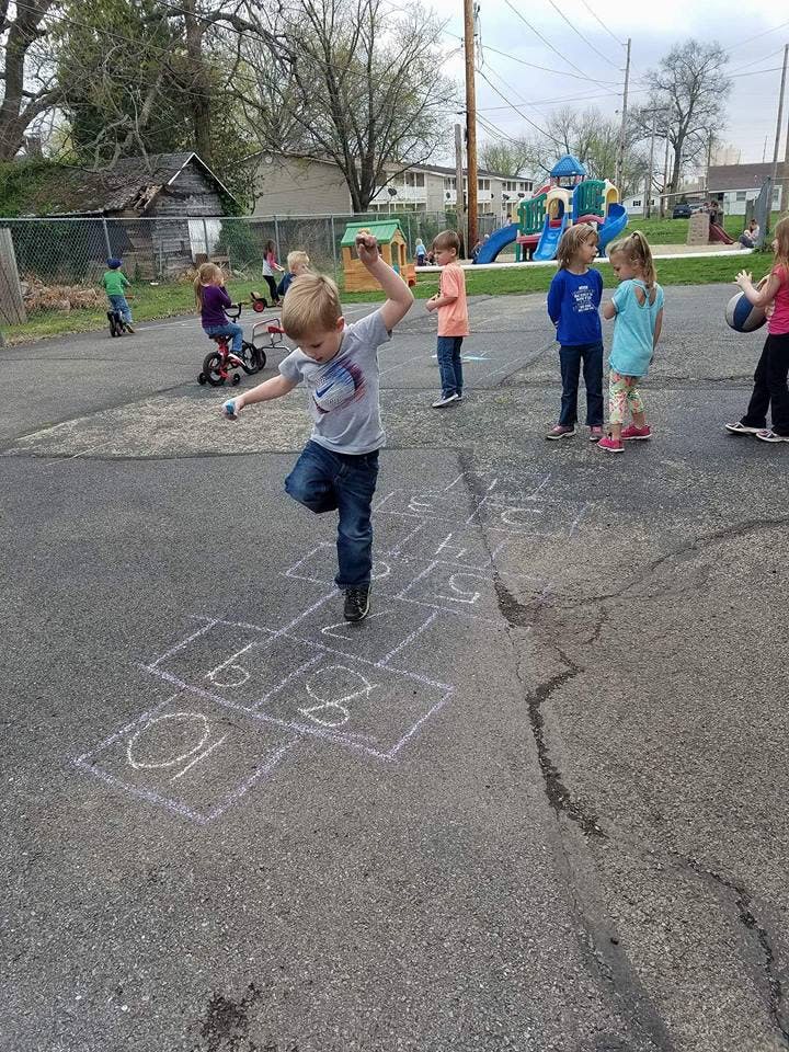 Child playing hopscotch on a paved surface with other children in the background