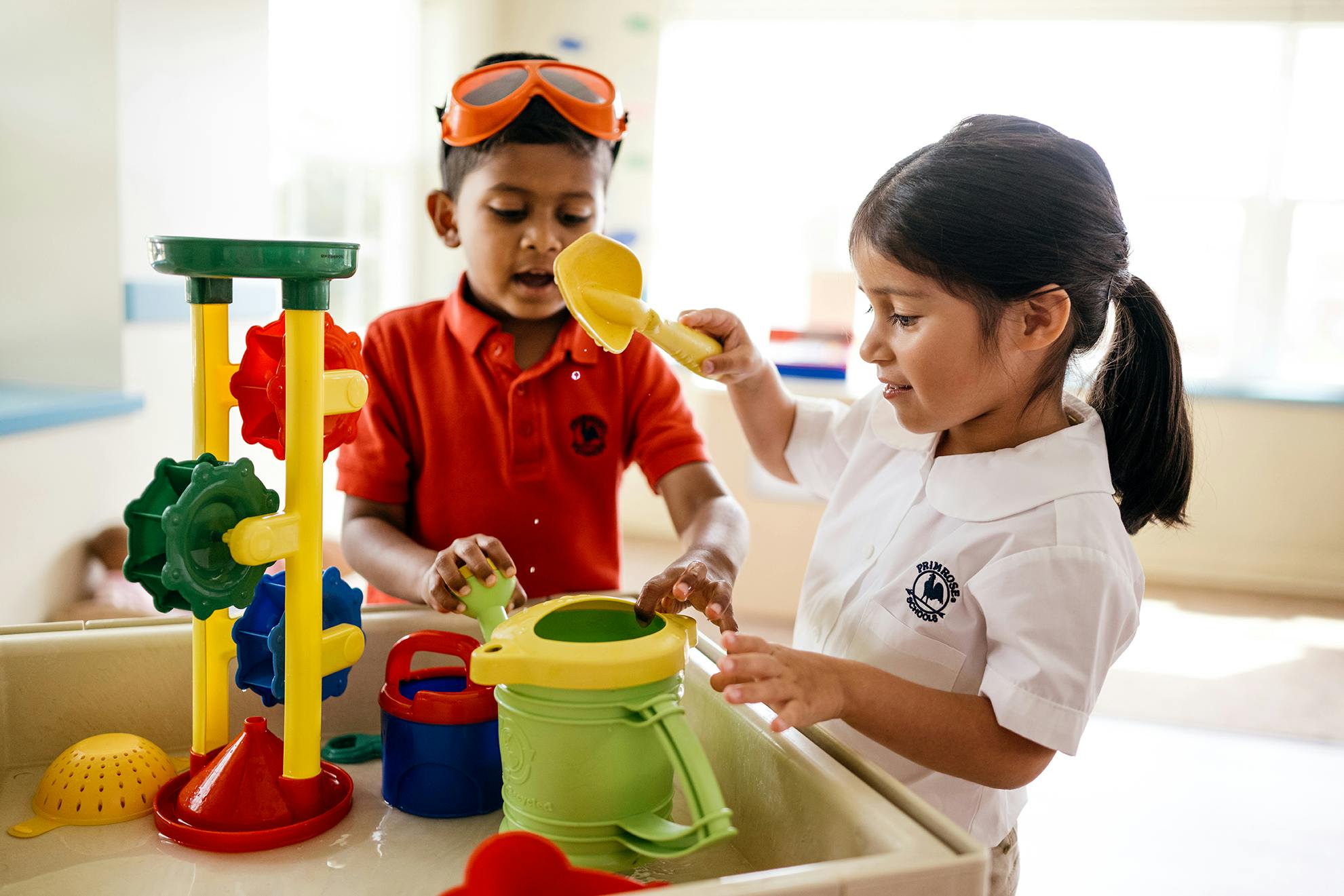 Two children playing with water toys in a sensory bin
