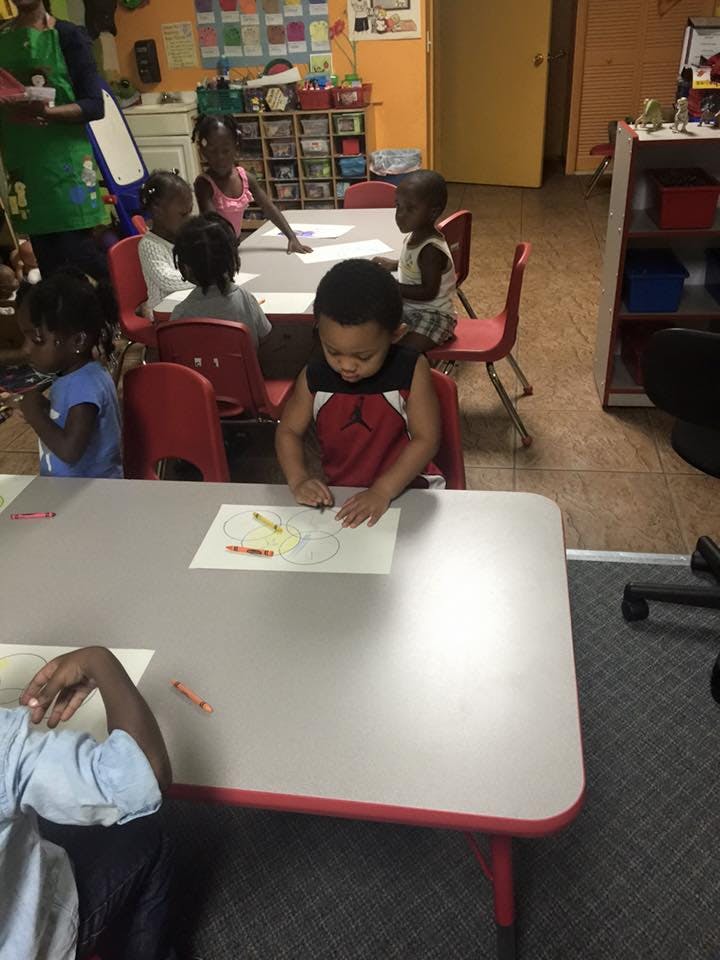 Child coloring at a table in a classroom with other children
