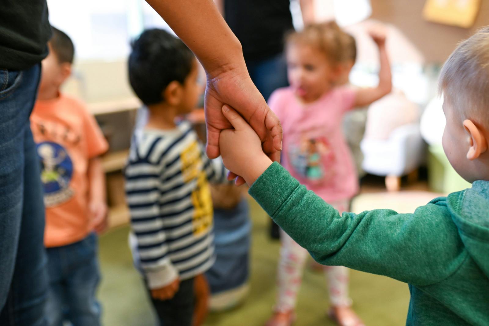 Adult holding a child's hand in a room with other children