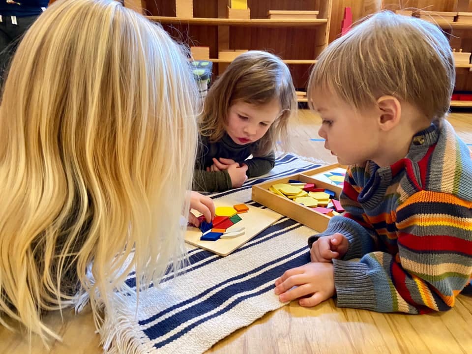 Three children playing with colorful geometric shapes on a mat