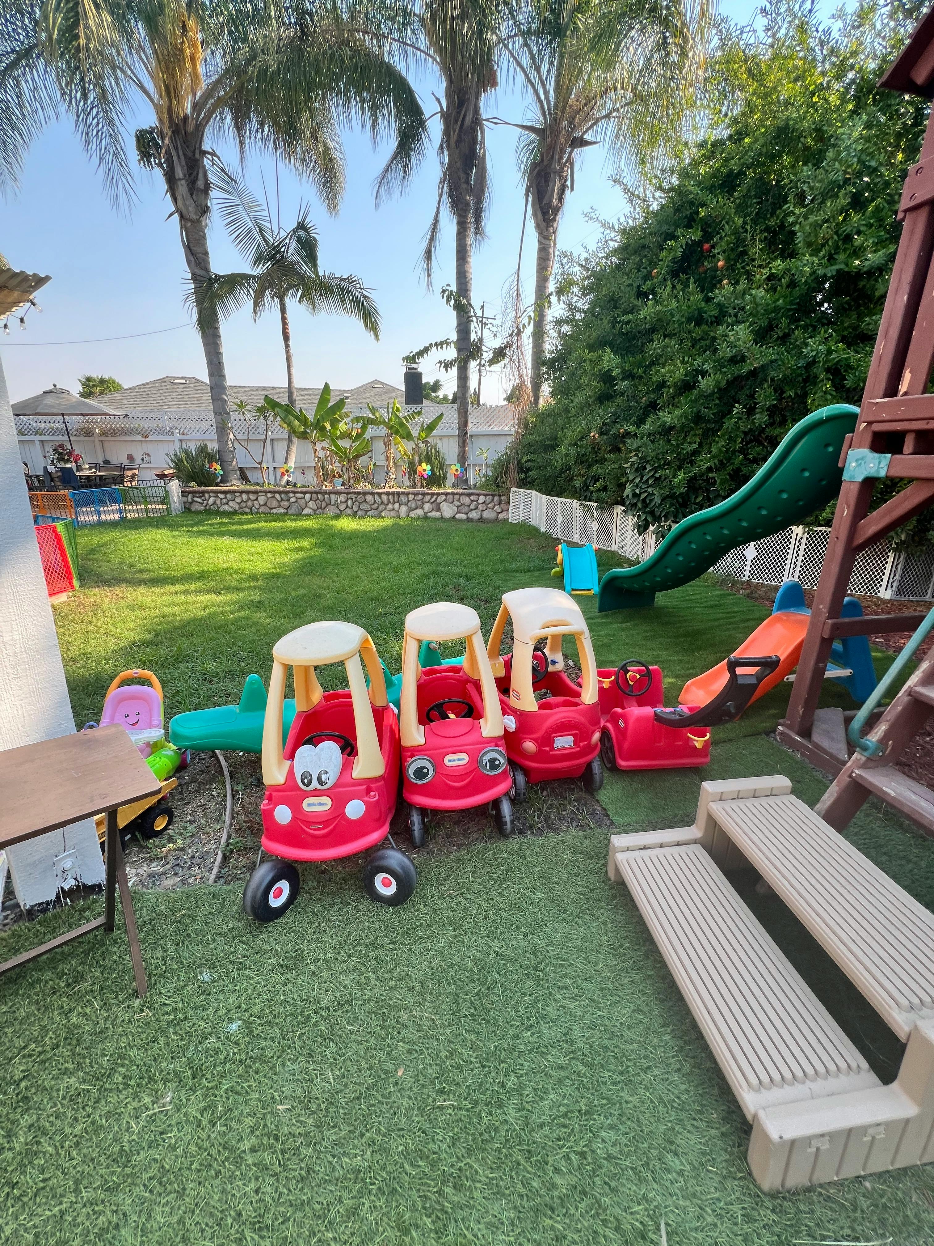 Three red toy cars on a grassy lawn with a green slide and play structure