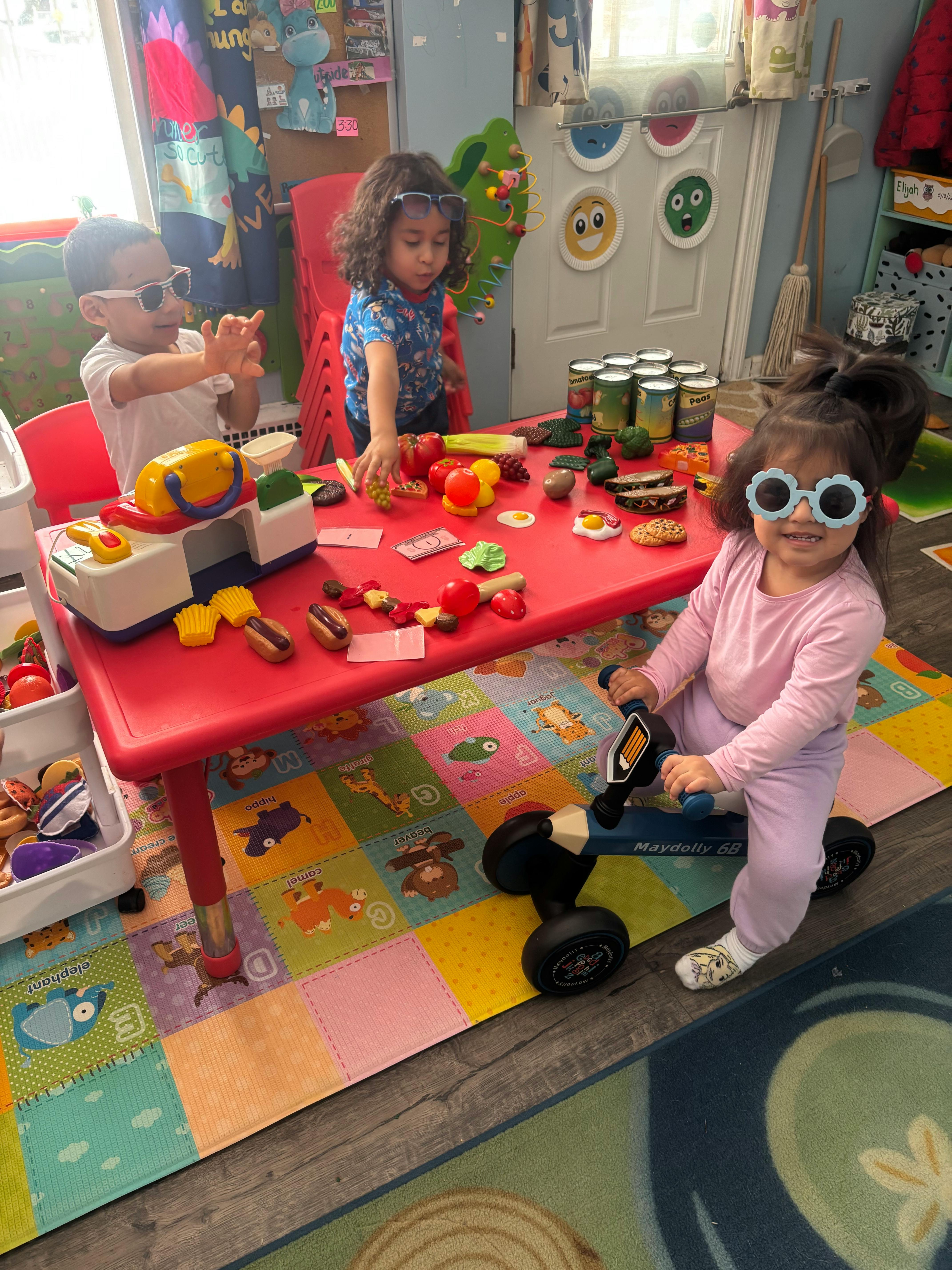 Three children playing with toys at a red table in a room