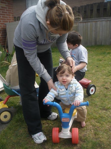 Person helping a child on a small riding toy in a grassy area