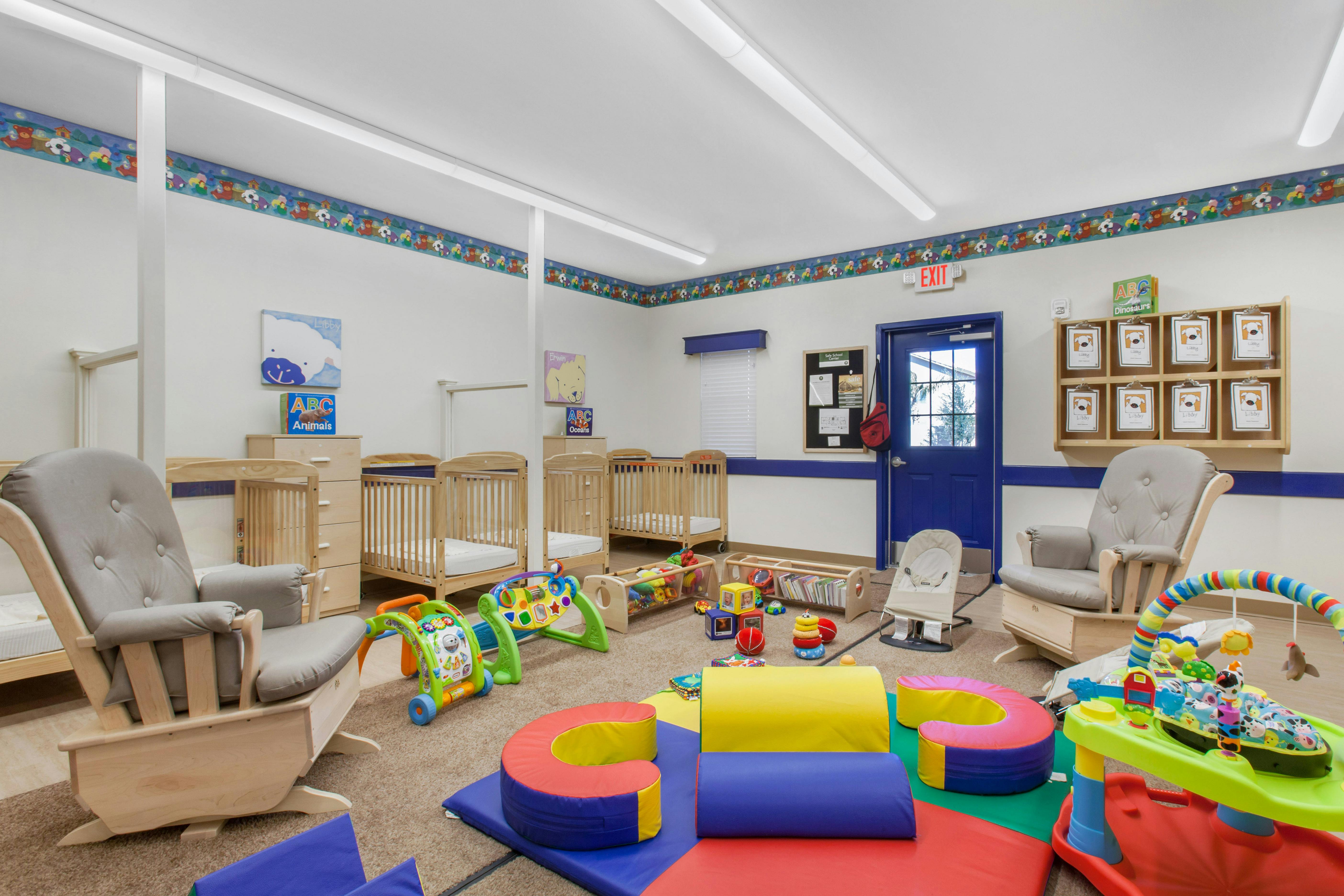 Baby nursery room with multiple cribs, a blue door, and infant play equipment