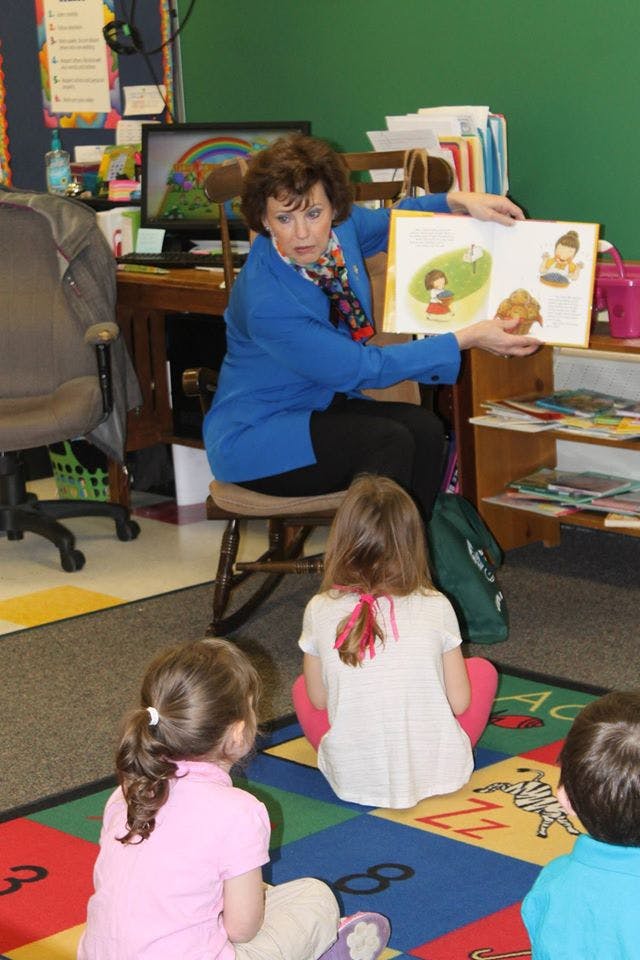 Person reading a book to children sitting on a colorful rug
