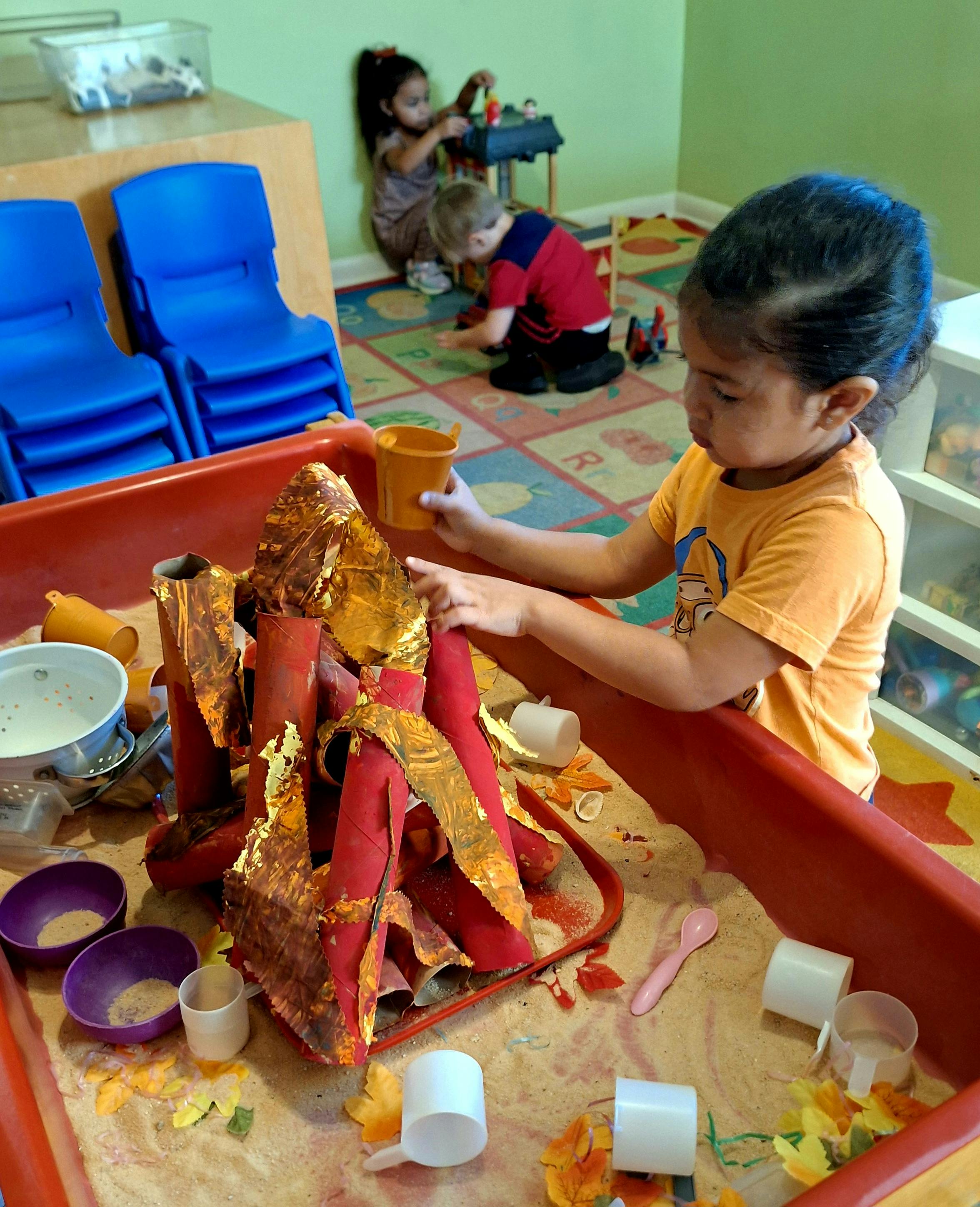 Child playing with a simulated campfire made of paper in a sensory sand table