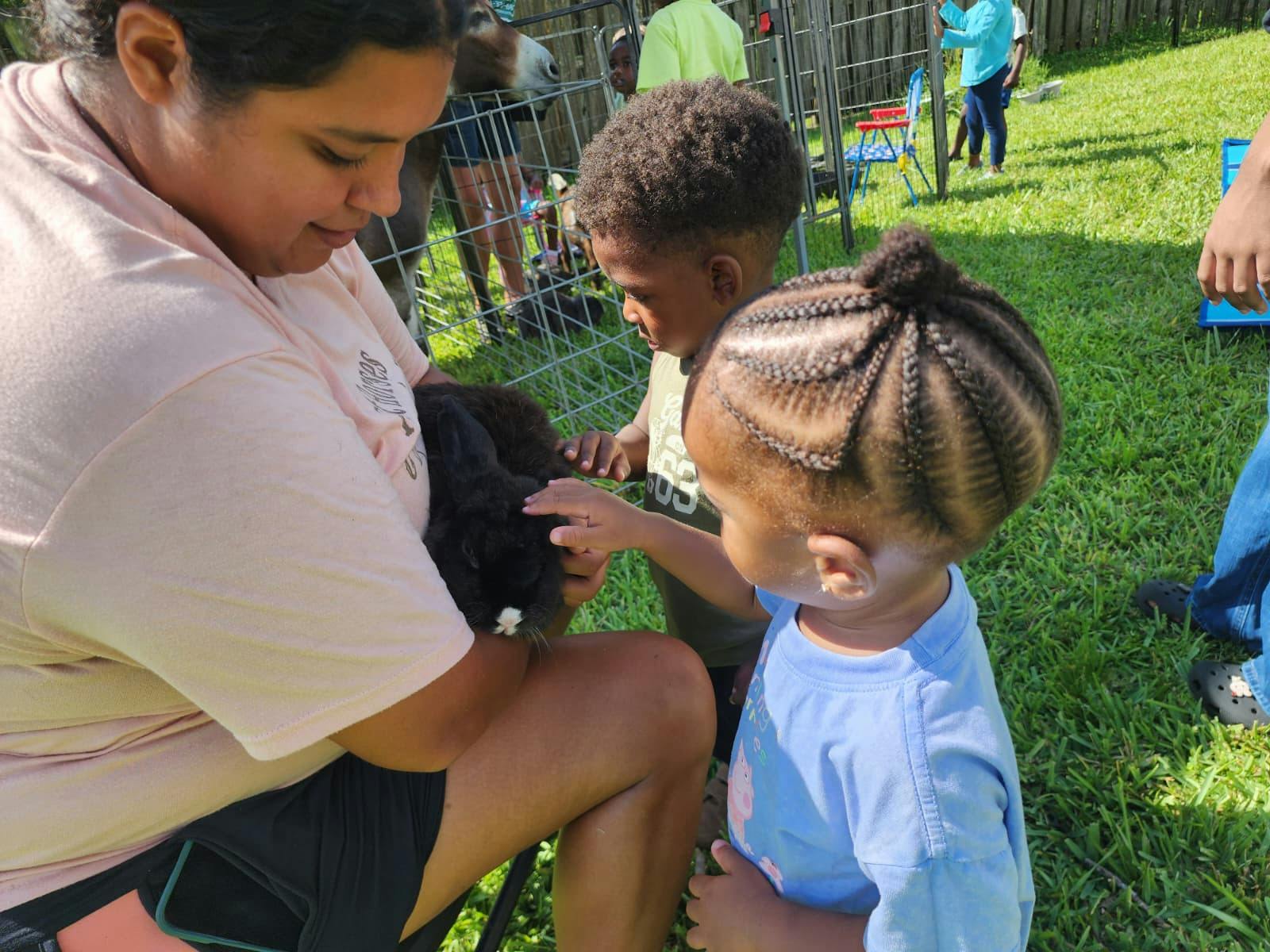 A person holding a rabbit while two children reach out to touch it