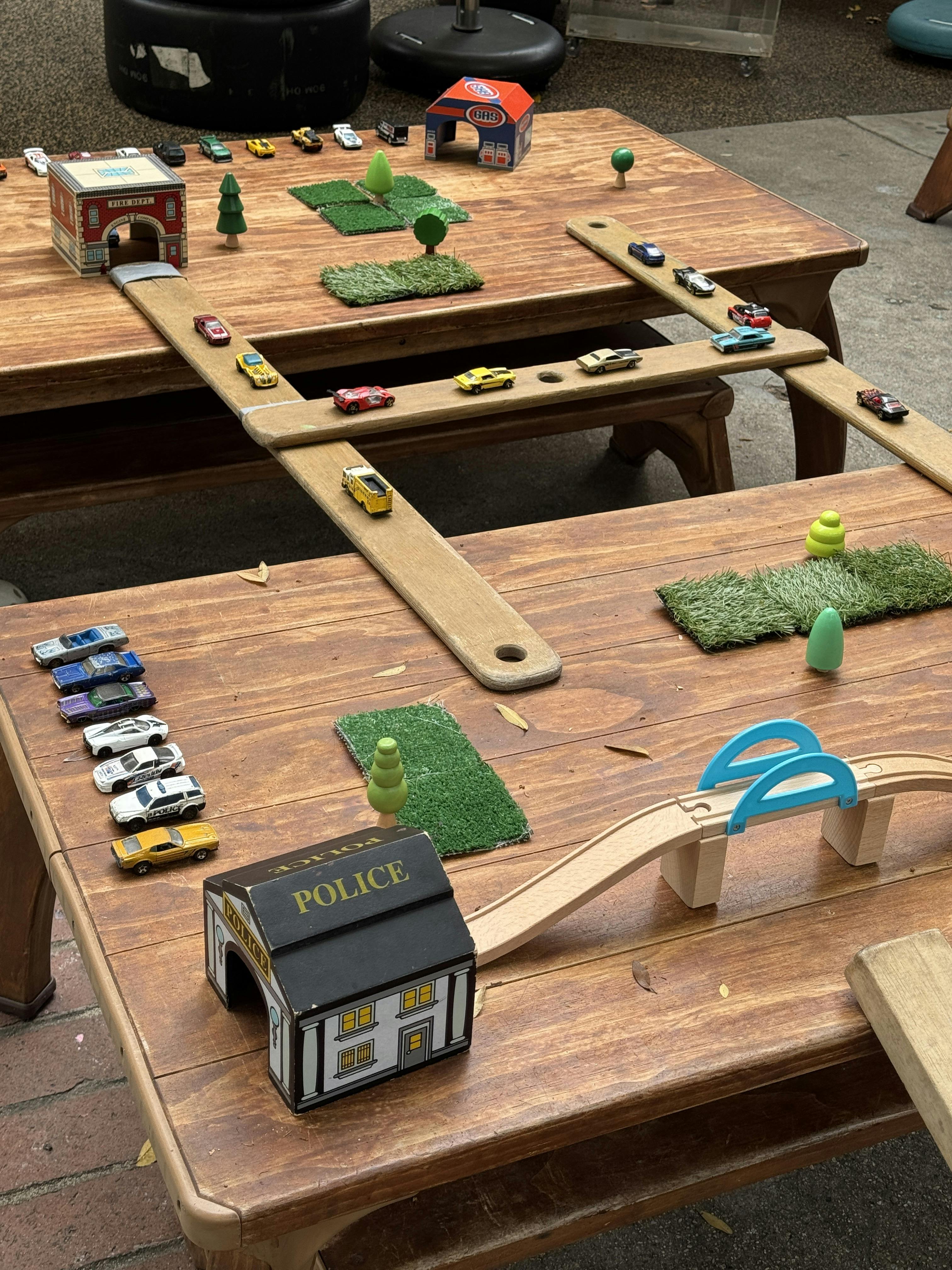 Toy cars and buildings on two wooden tables connected by ramps