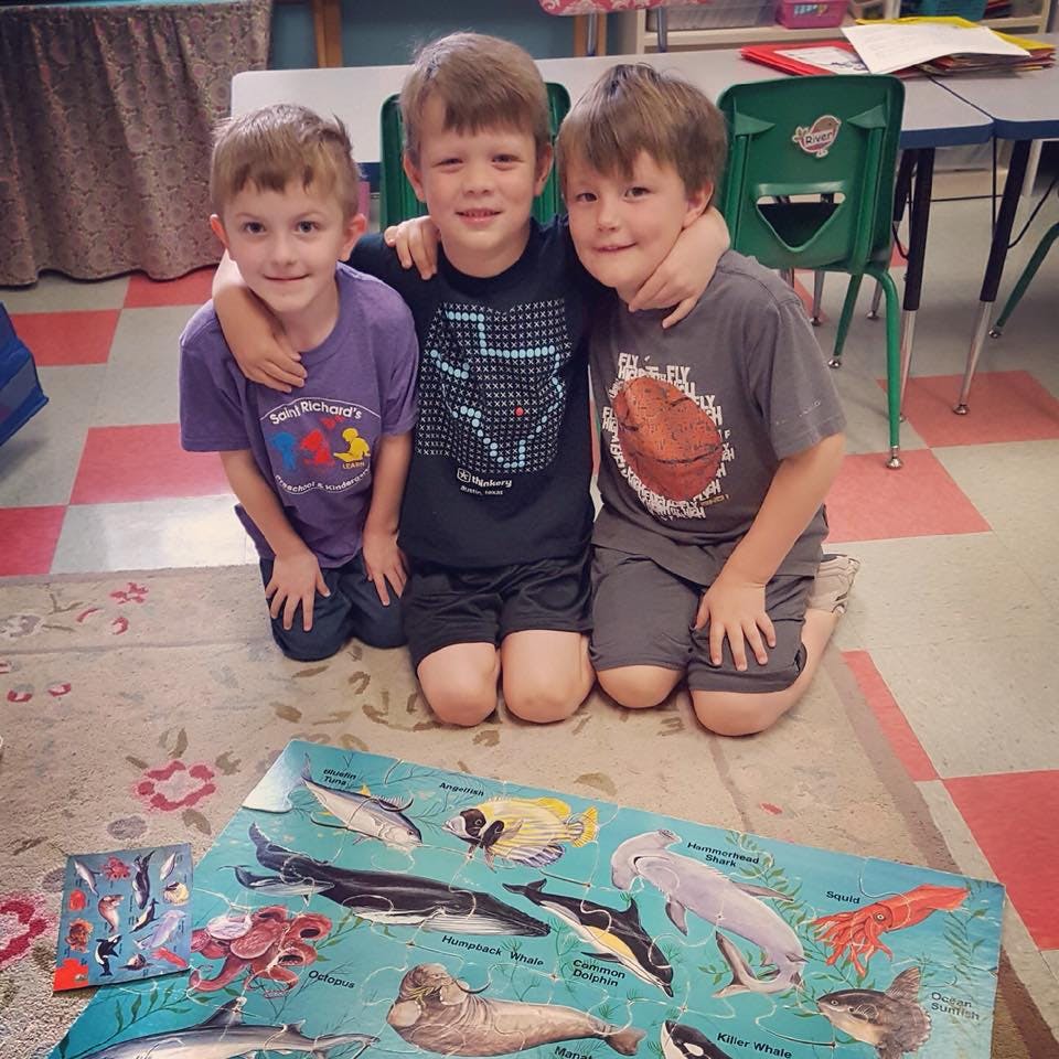 Three children kneeling on a rug with arms around each other, a marine life poster in front