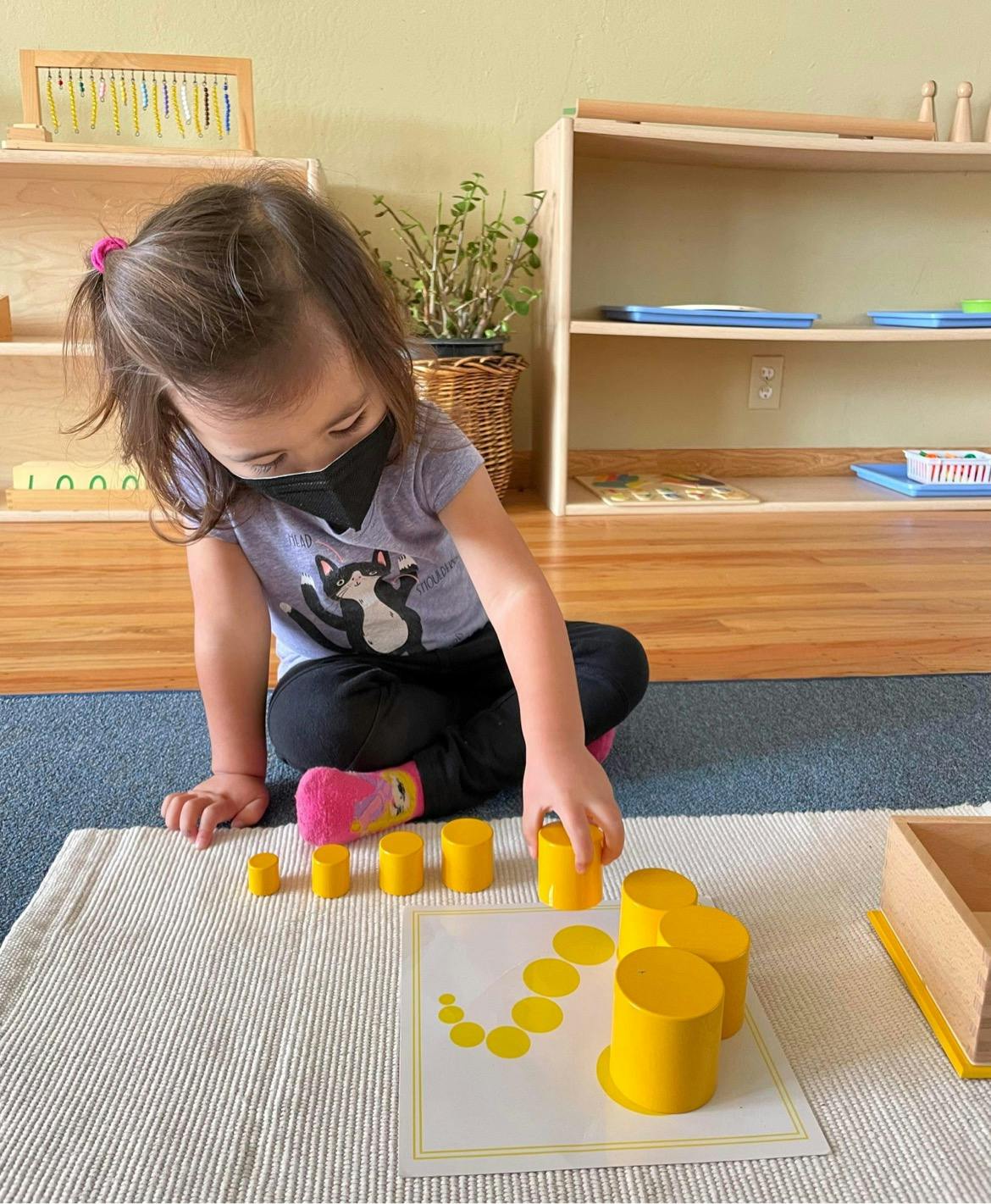Child playing with yellow cylindrical blocks on a mat