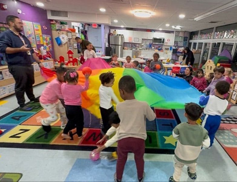 Group of children playing with a colorful parachute in a classroom