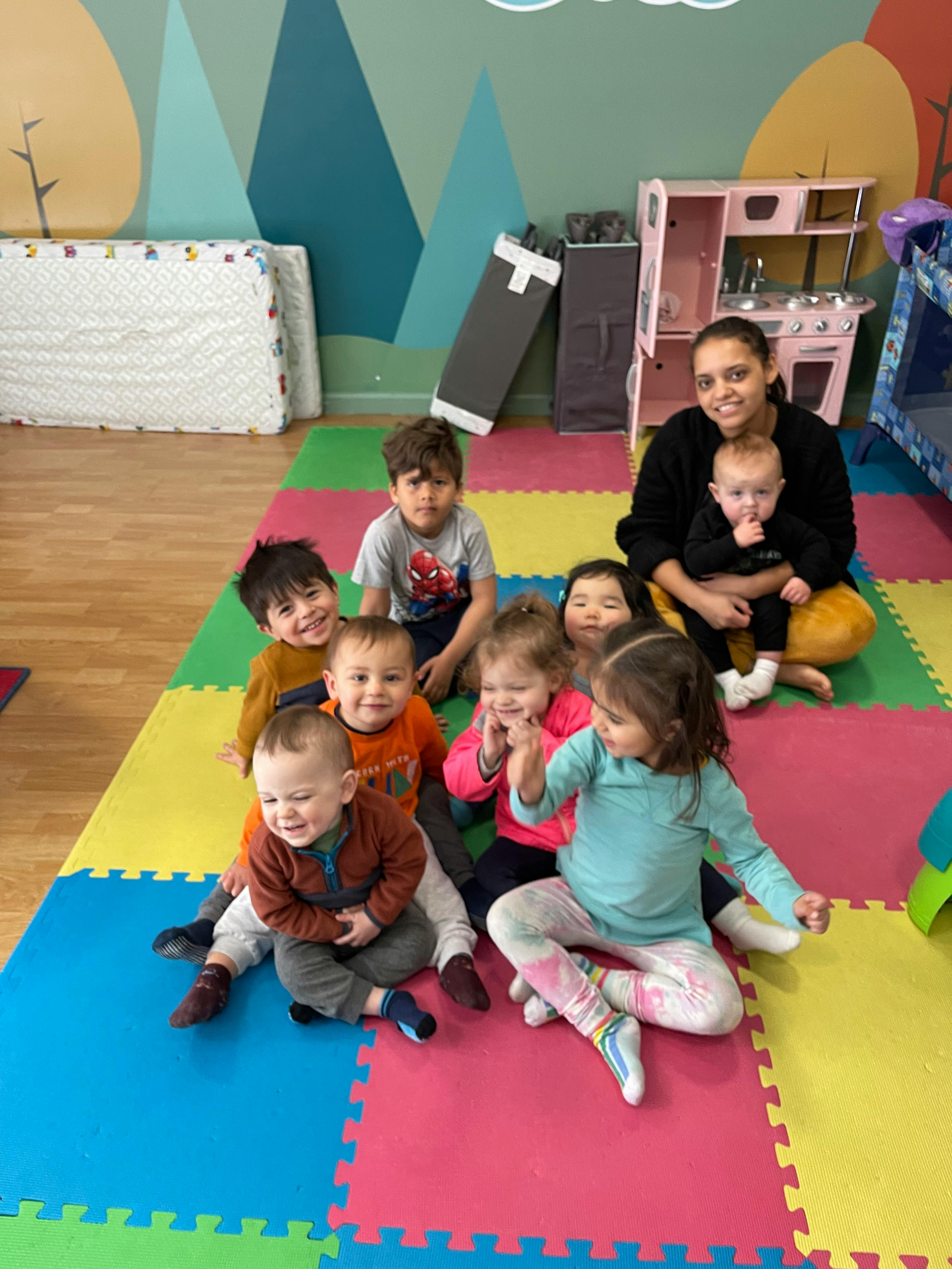 Adult and multiple children sitting on a colorful mat in a play area