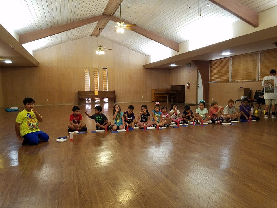 Children sitting on a wooden floor in a large room