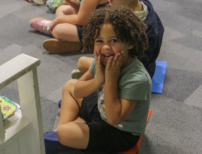 Child sitting on floor with hands on face, smiling