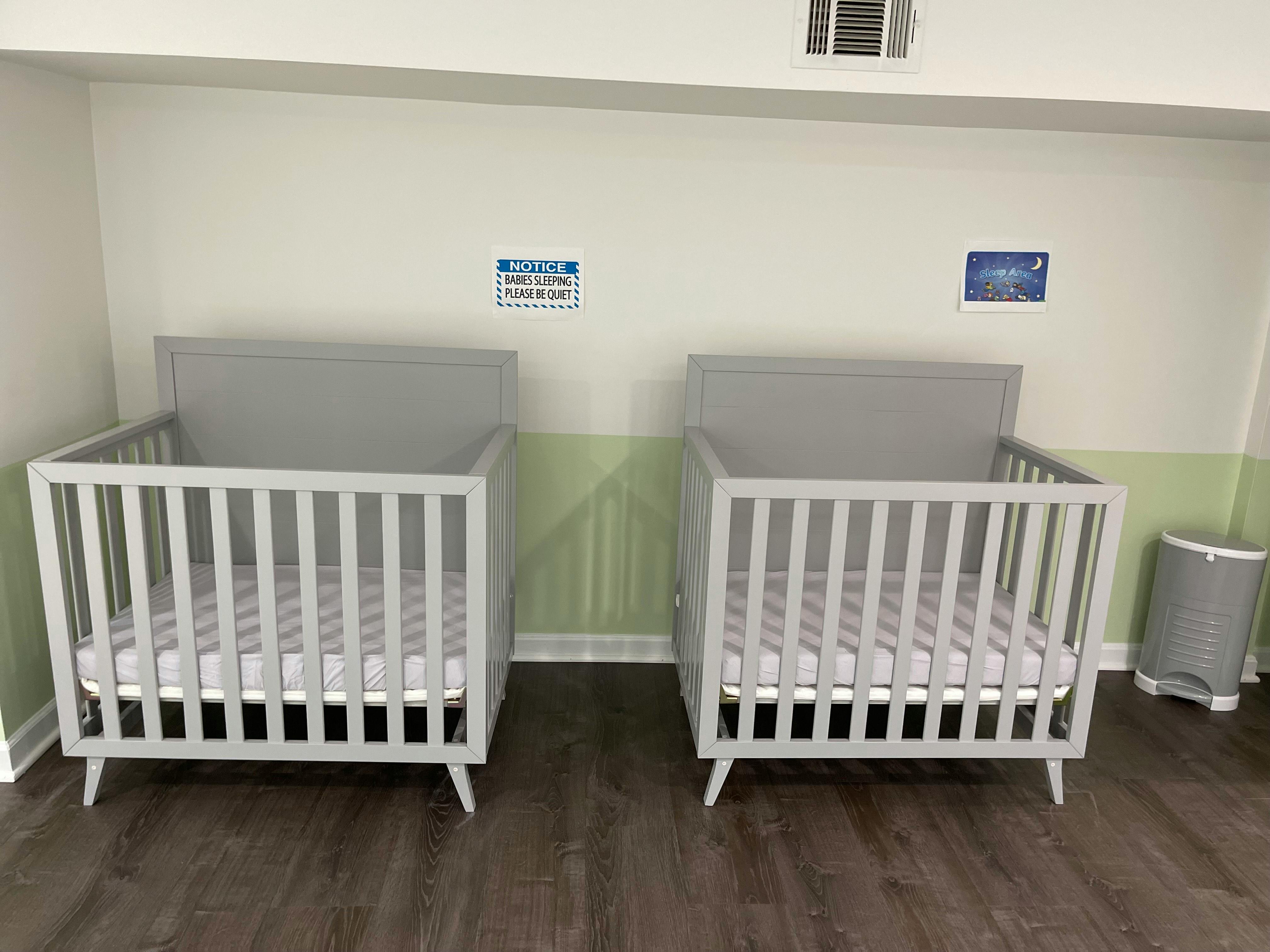 Two empty cribs with mattresses in a room