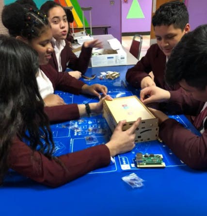 Teens assembling a wooden box with electronic components on a blue table
