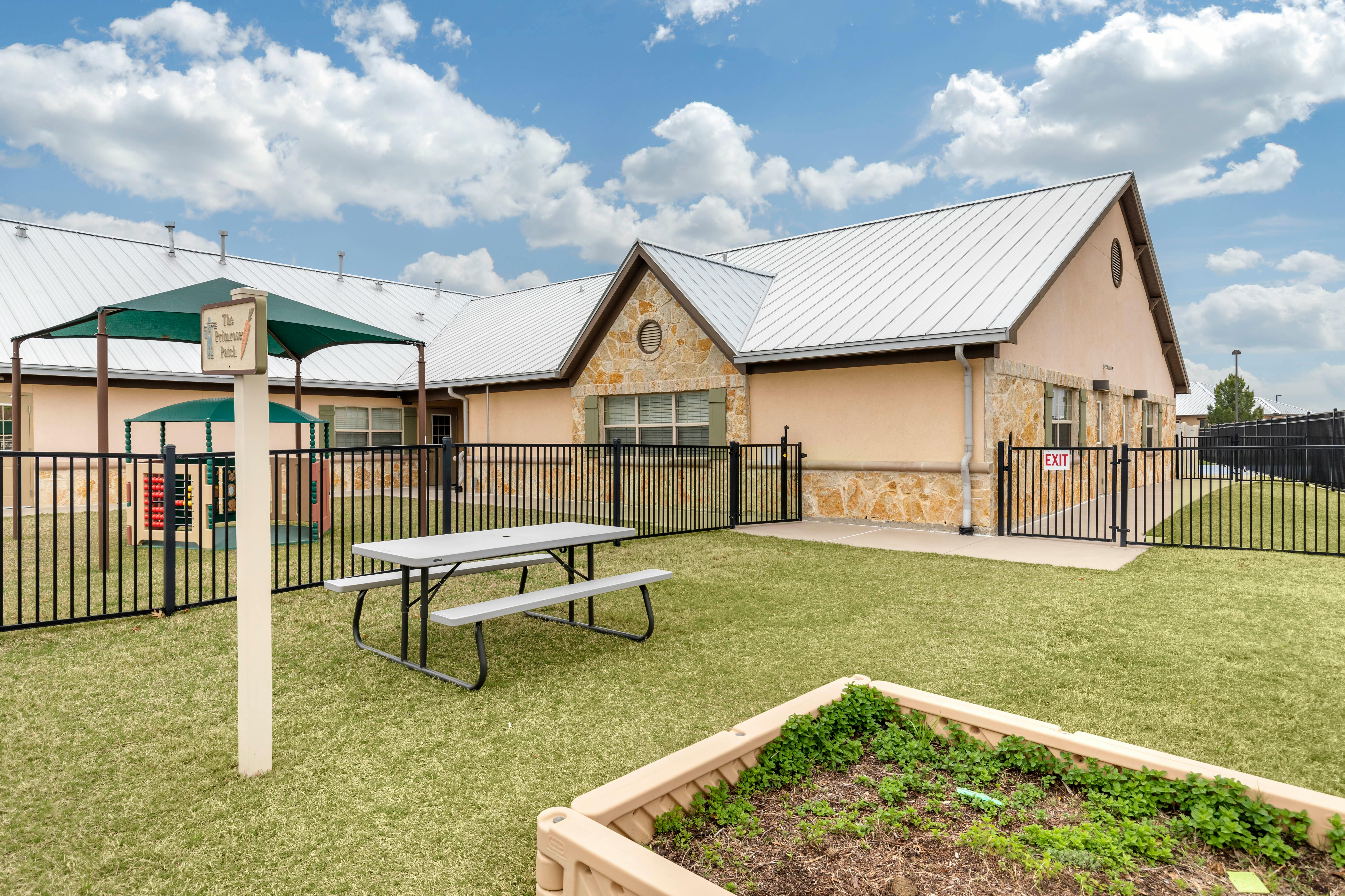 Playground area with a picnic table, fenced-in play structure, and building