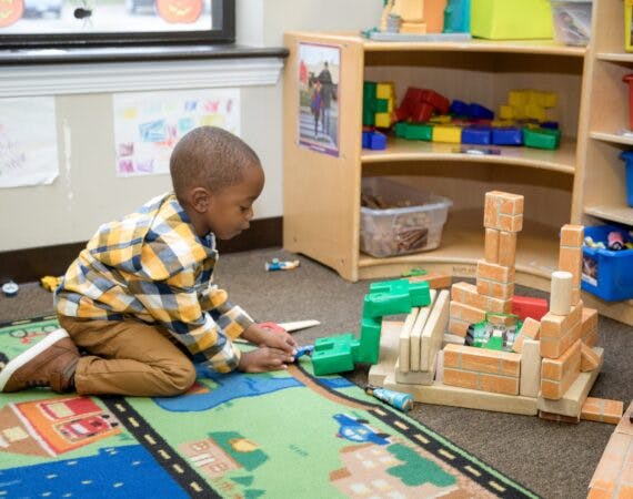 Child playing with blocks on a rug in a classroom