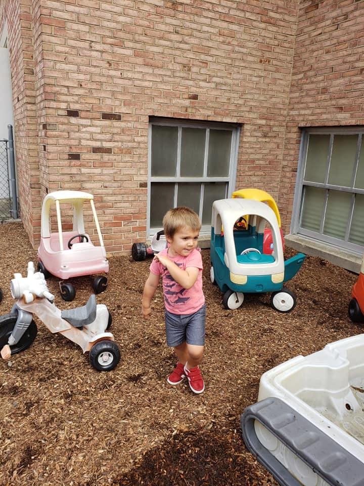 Child standing on wood chips near toy cars