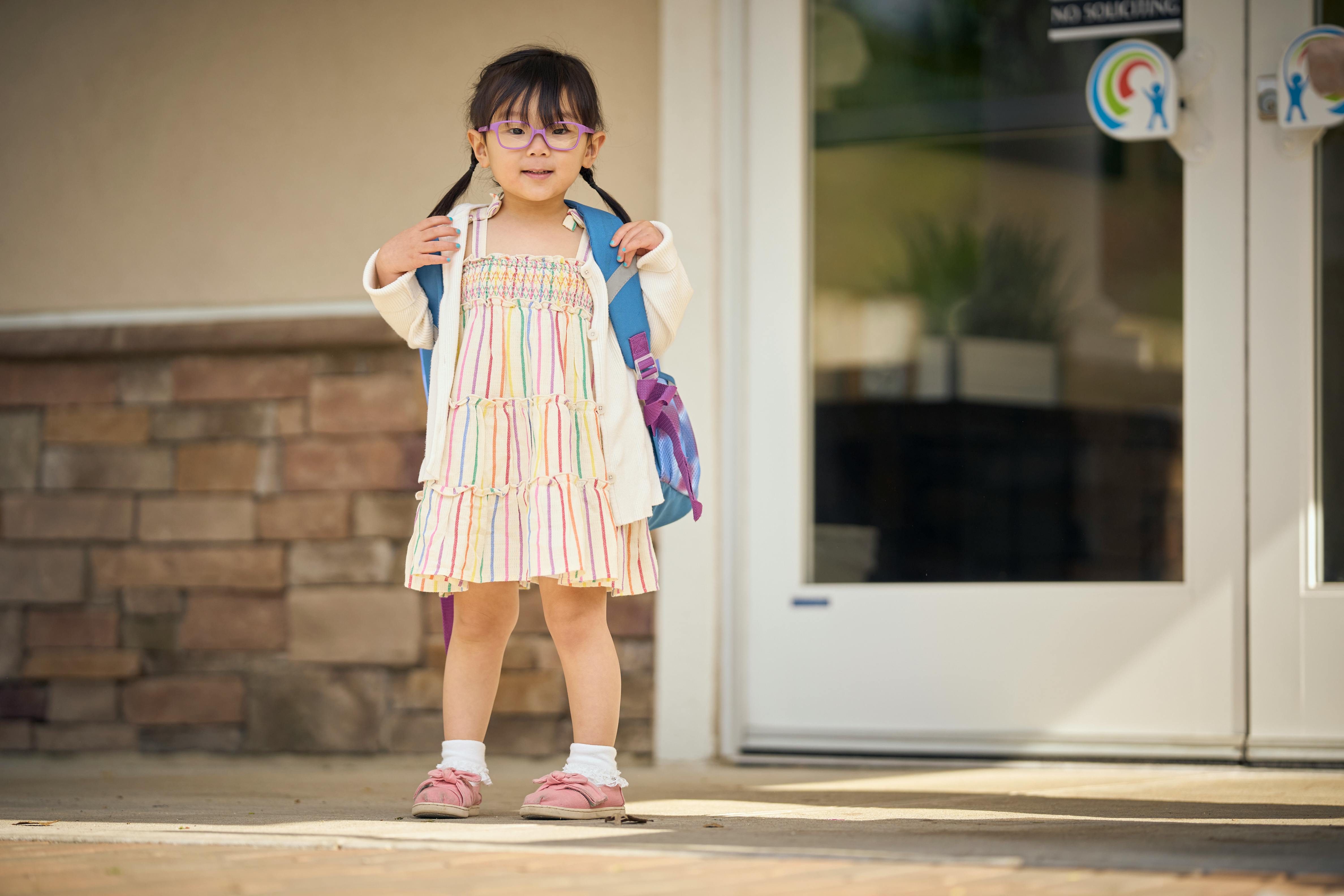 Child wearing glasses and backpack standing in front of a door