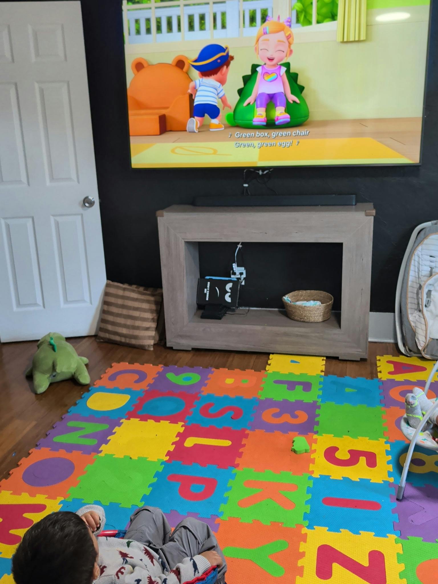 Child lying on a colorful foam alphabet play mat watching a cartoon on a TV