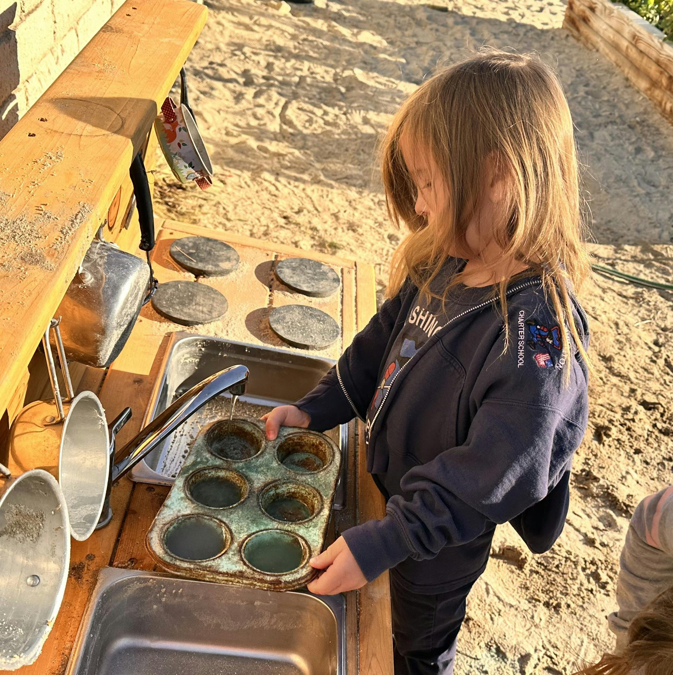 Child playing with a muffin tin at an outdoor play kitchen
