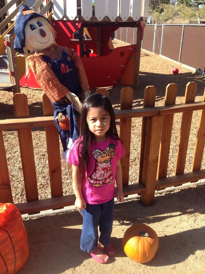 Child standing next to a scarecrow and a pumpkin