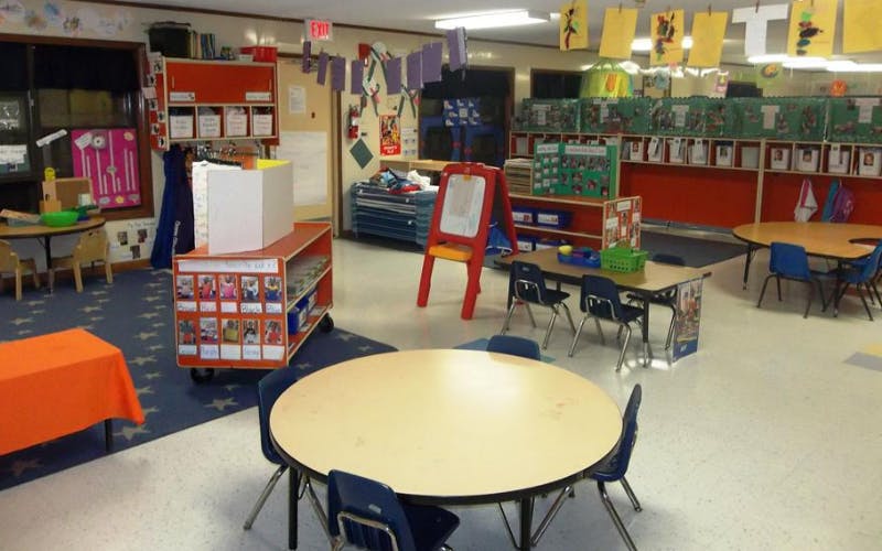 Empty classroom with multiple tables, chairs, and learning materials