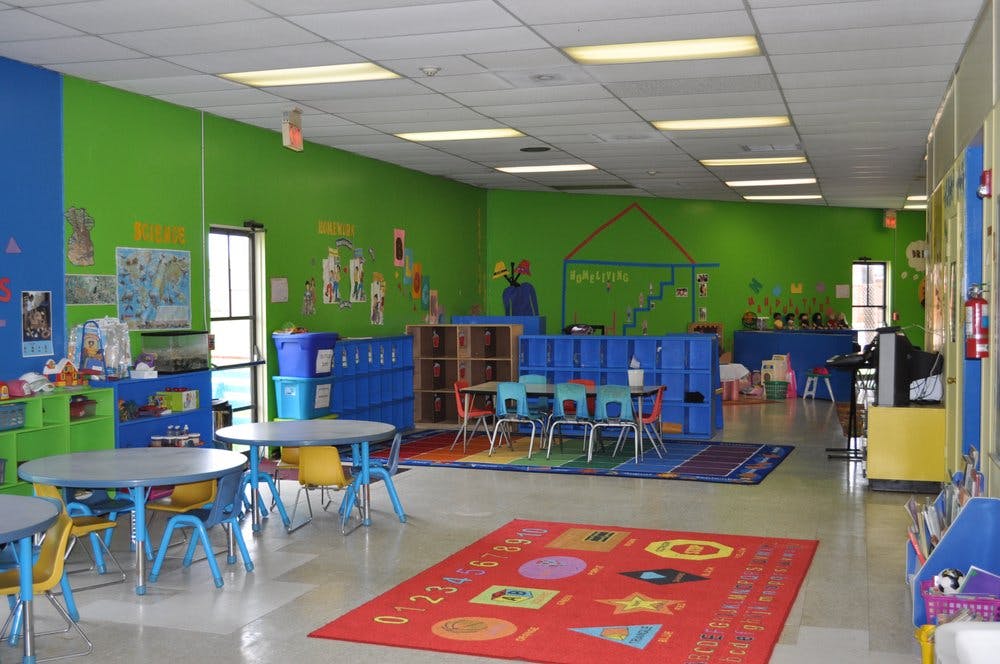 Classroom with small tables and chairs, colorful walls, and a red rug
