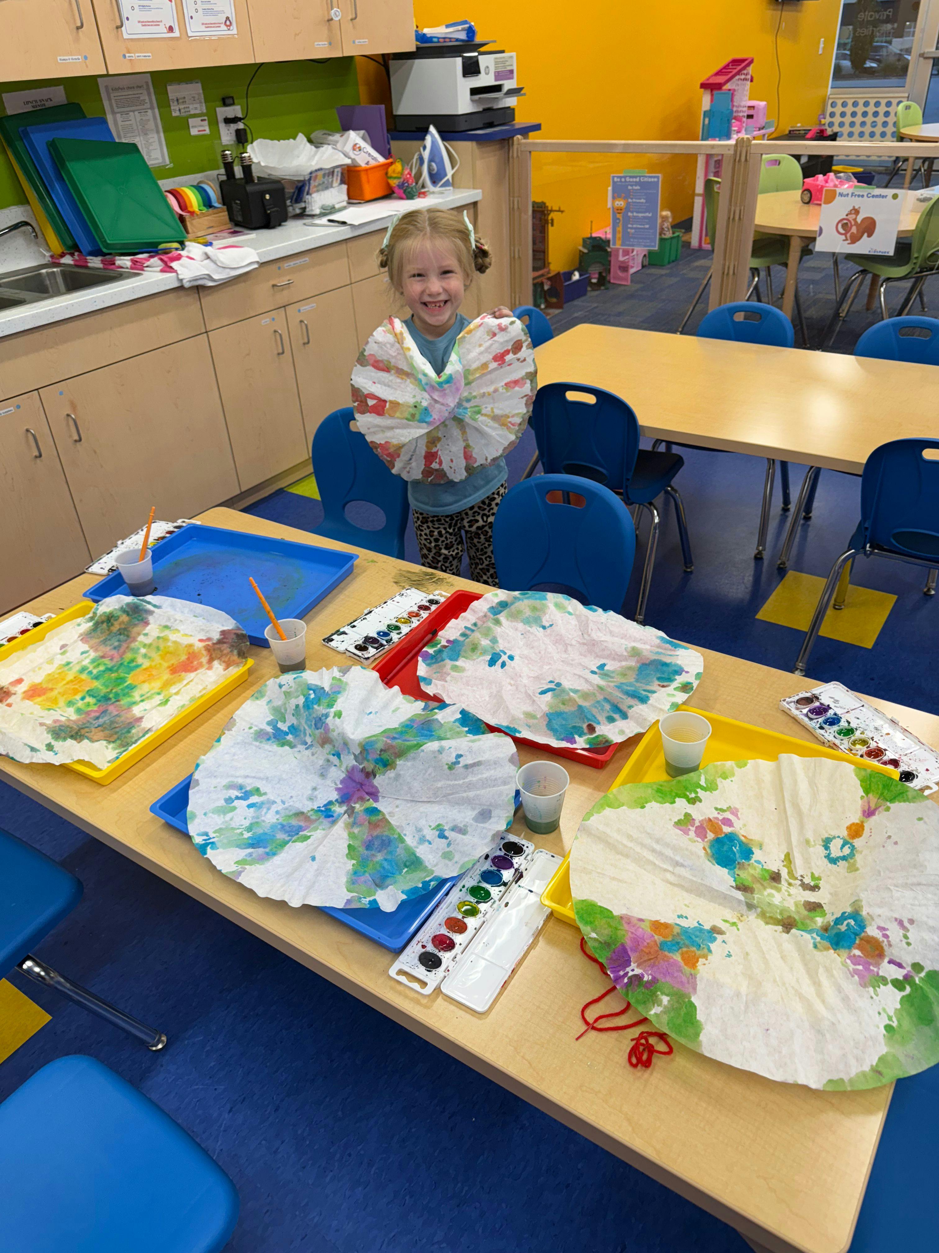 Child in a classroom holding up a colorful painted paper project