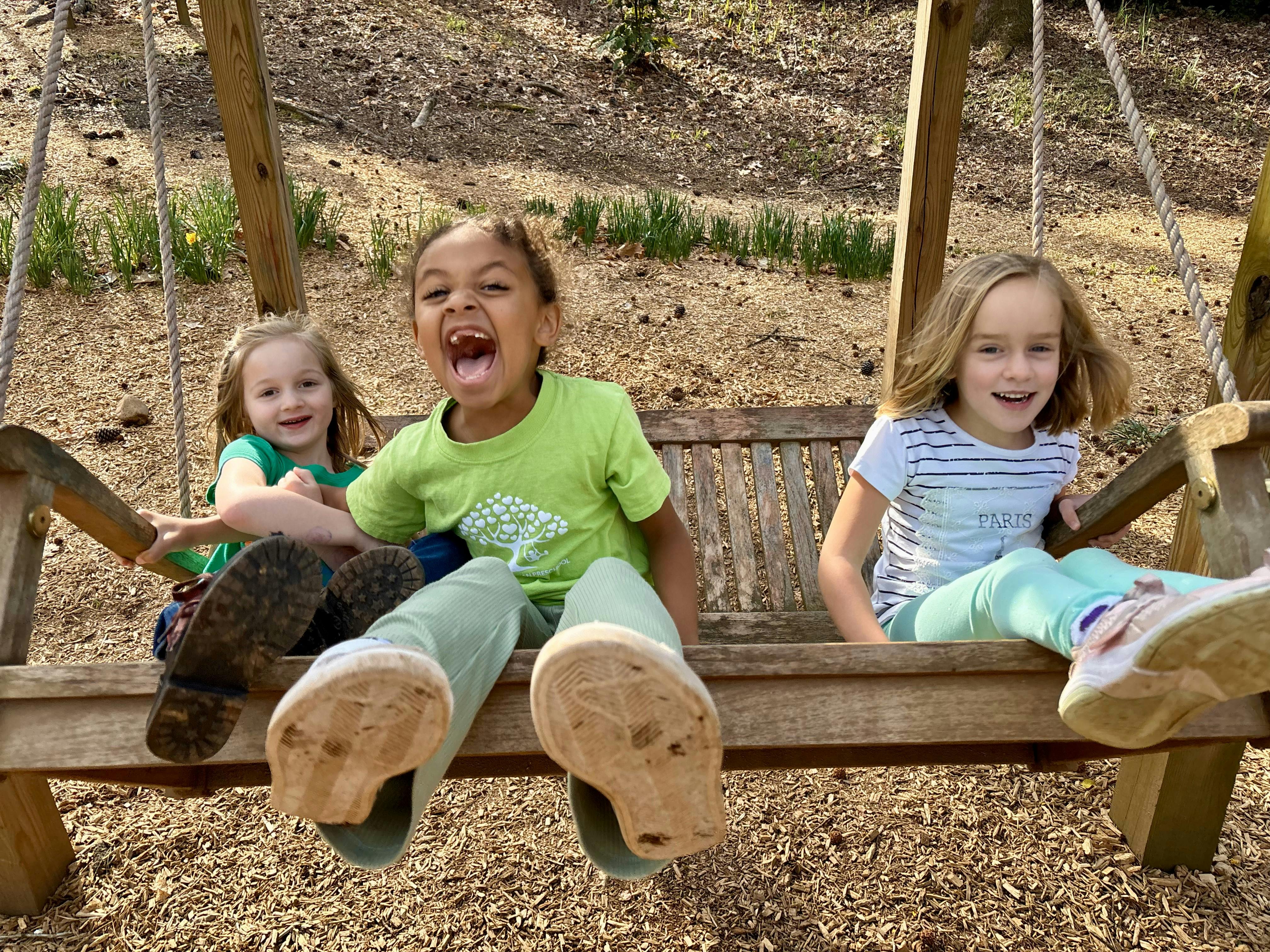 Three children sitting on a wooden swing